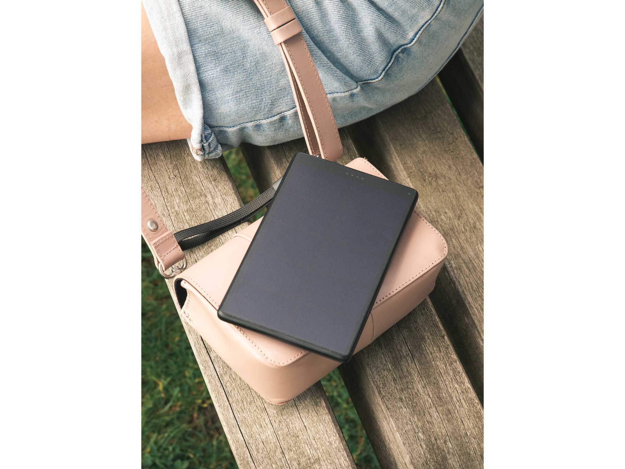 Ein Tablet liegt auf einer Handtasche auf einer Parkbank. Der Hintergrund ist grün verschwommen.