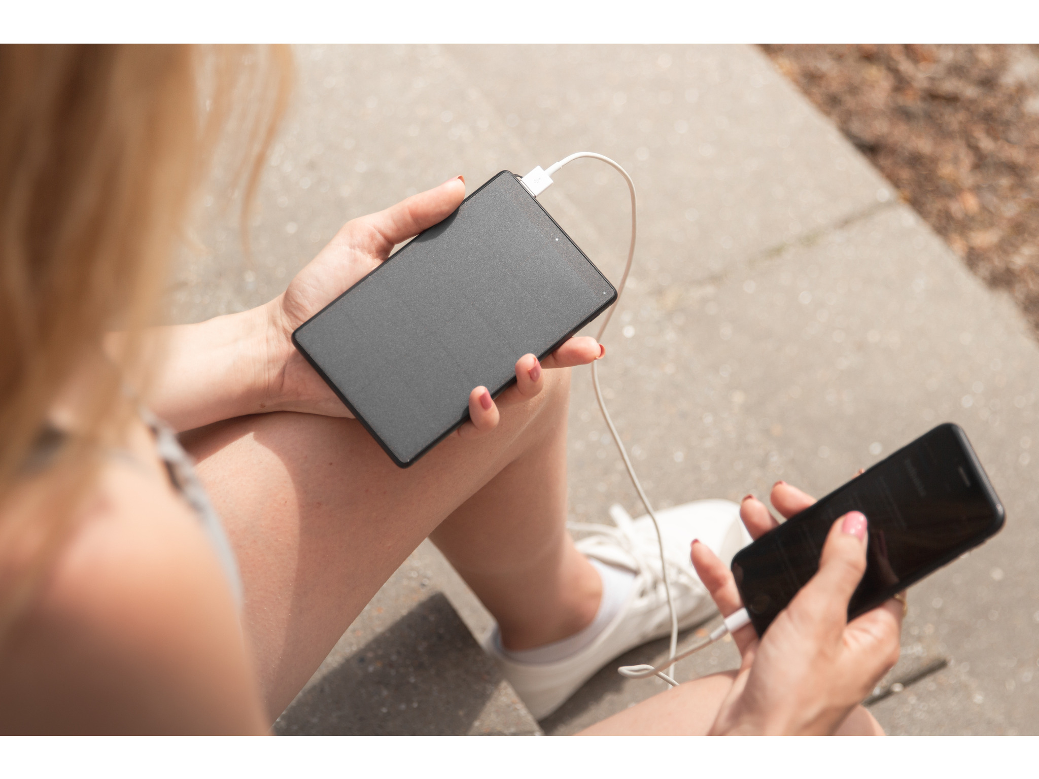Eine Frau, die eine schwarze Powerbank und ein Telefon hält, das draußen daran aufgeladen wird.