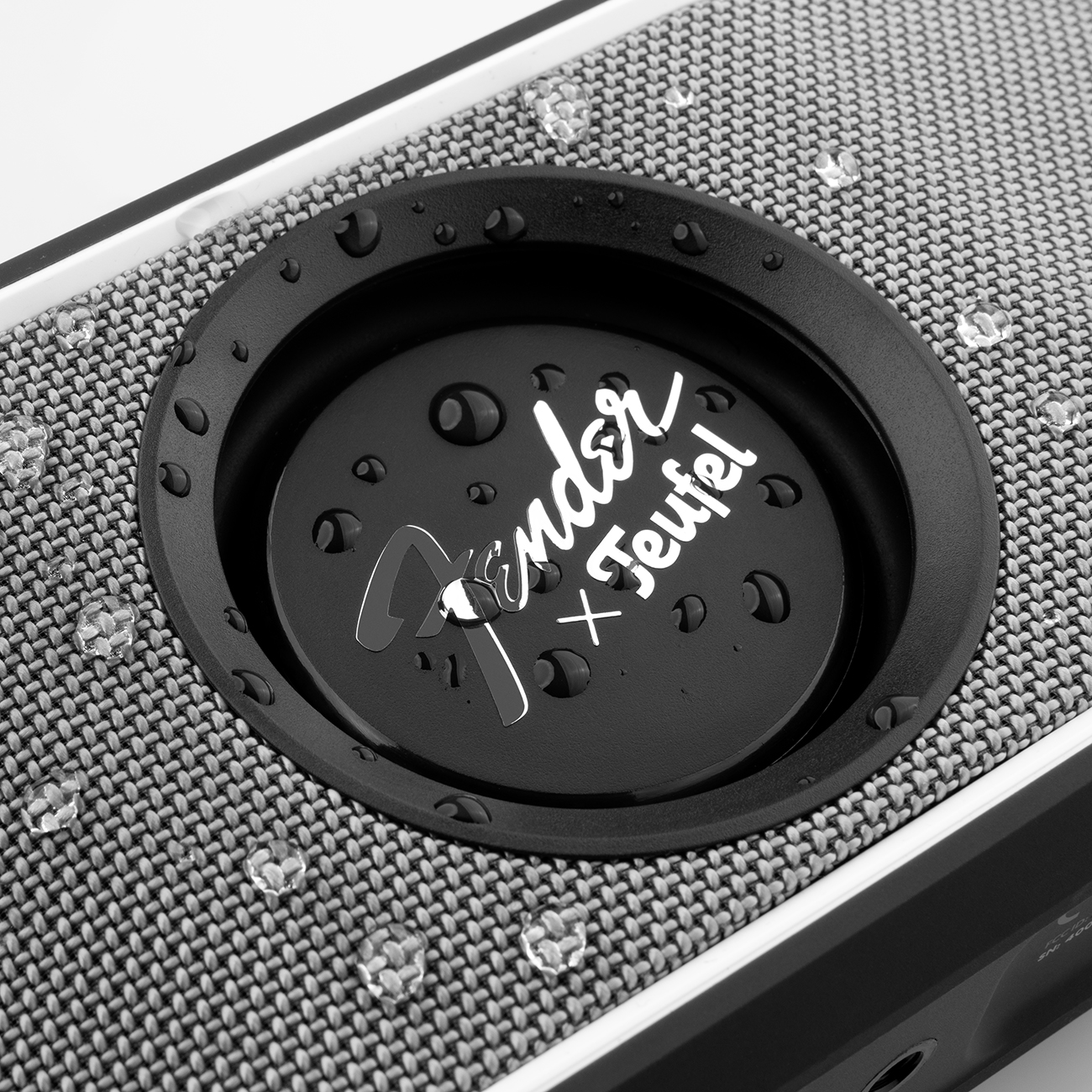 Close-up van een luidspreker. Zwart met zilveren logo. Waterdruppels erop.