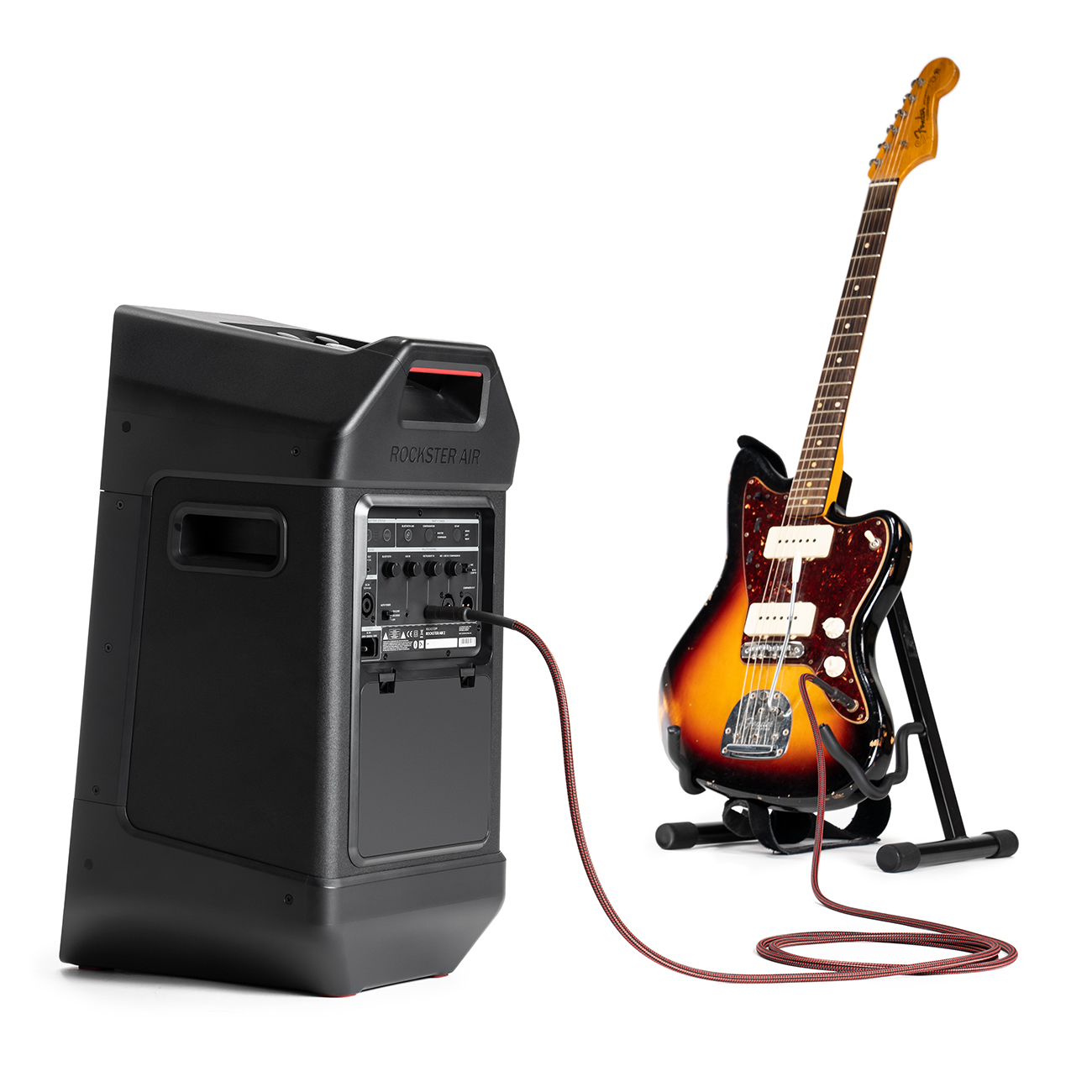 Een zwarte luidspreker en een sunburst gitaar op een standaard, verbonden door een rode kabel, op een witte achtergrond.