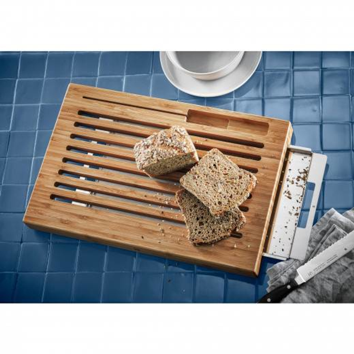 Ein hölzernes Brotbrett mit Brot und einem Messer. Das Brett liegt auf einer blauen Fliesenoberfläche.