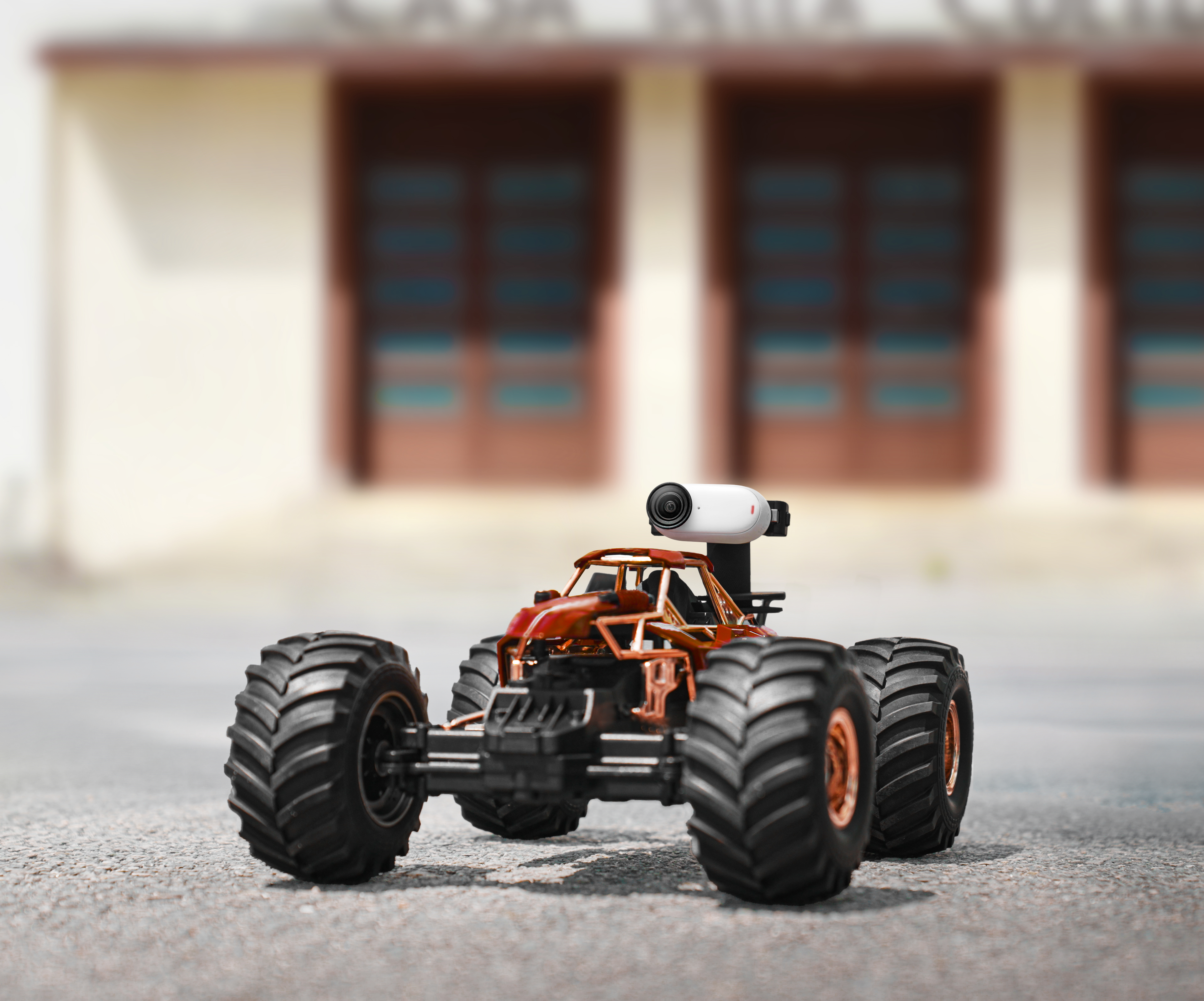Pomarańczowy i brązowy zdalnie sterowany samochód z dużymi oponami. Ma małą kamerę zamontowaną na górze.