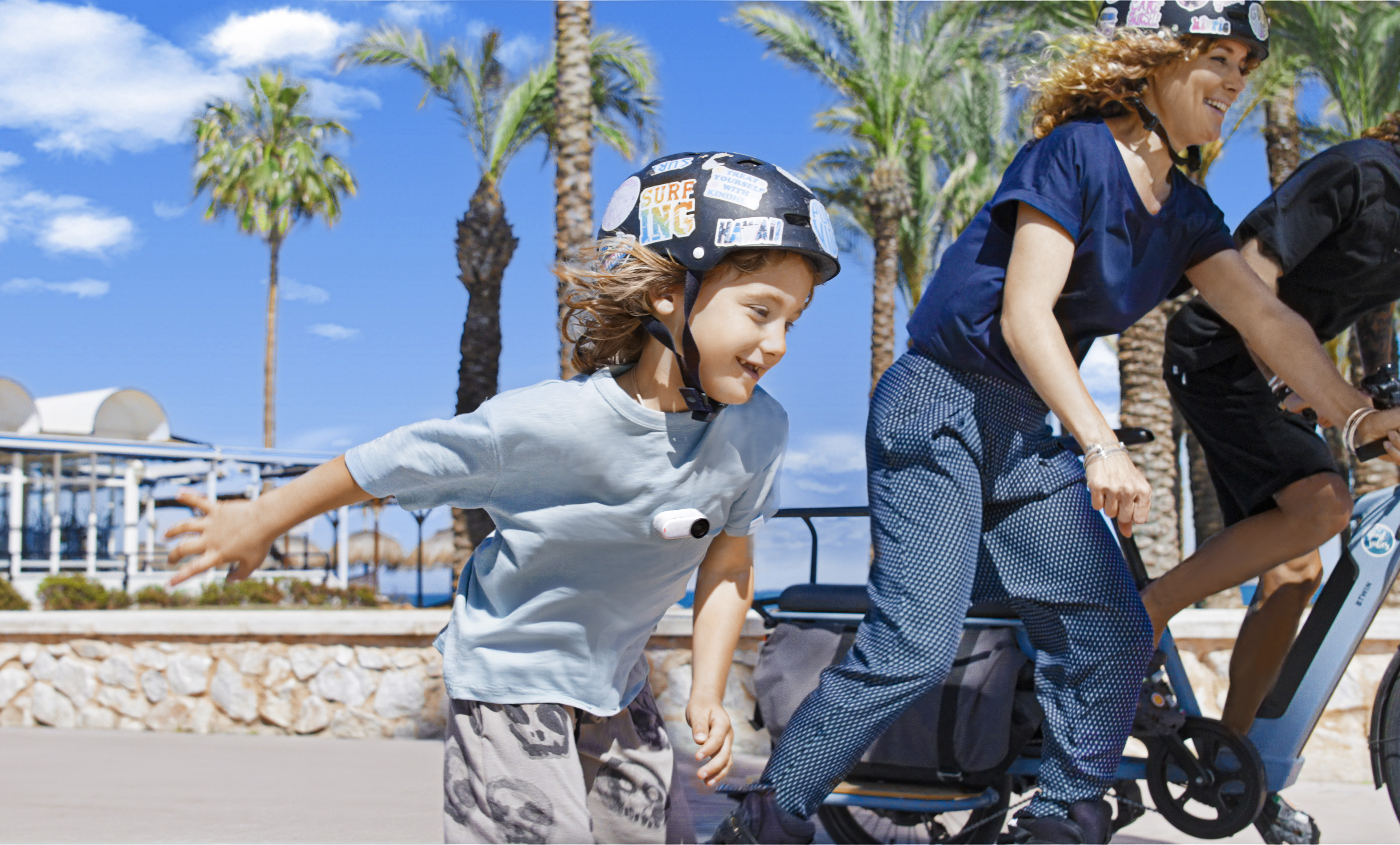 Chłopiec jeżdżący na rolkach z innymi. Ma na sobie kask. Słoneczny dzień, błękitne niebo, przed plażą.