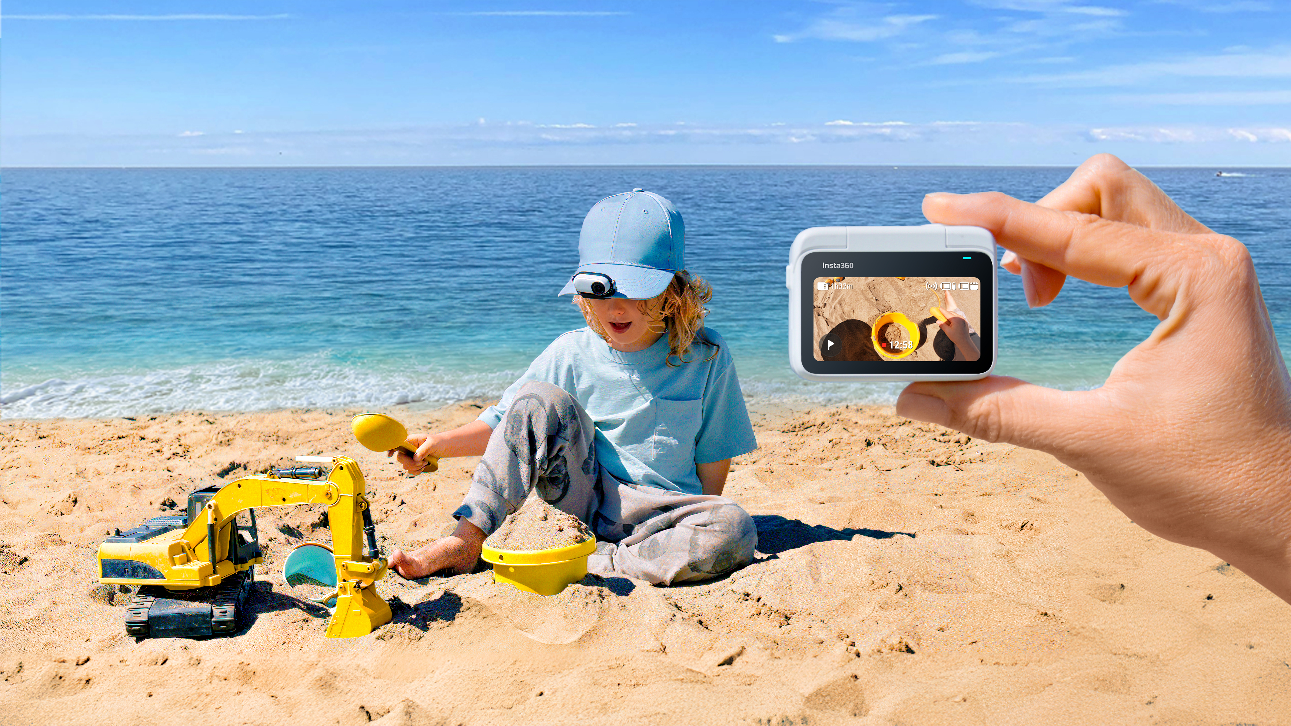 Dziecko bawiące się na plaży zabawką i ręka trzymająca ekran kamery.