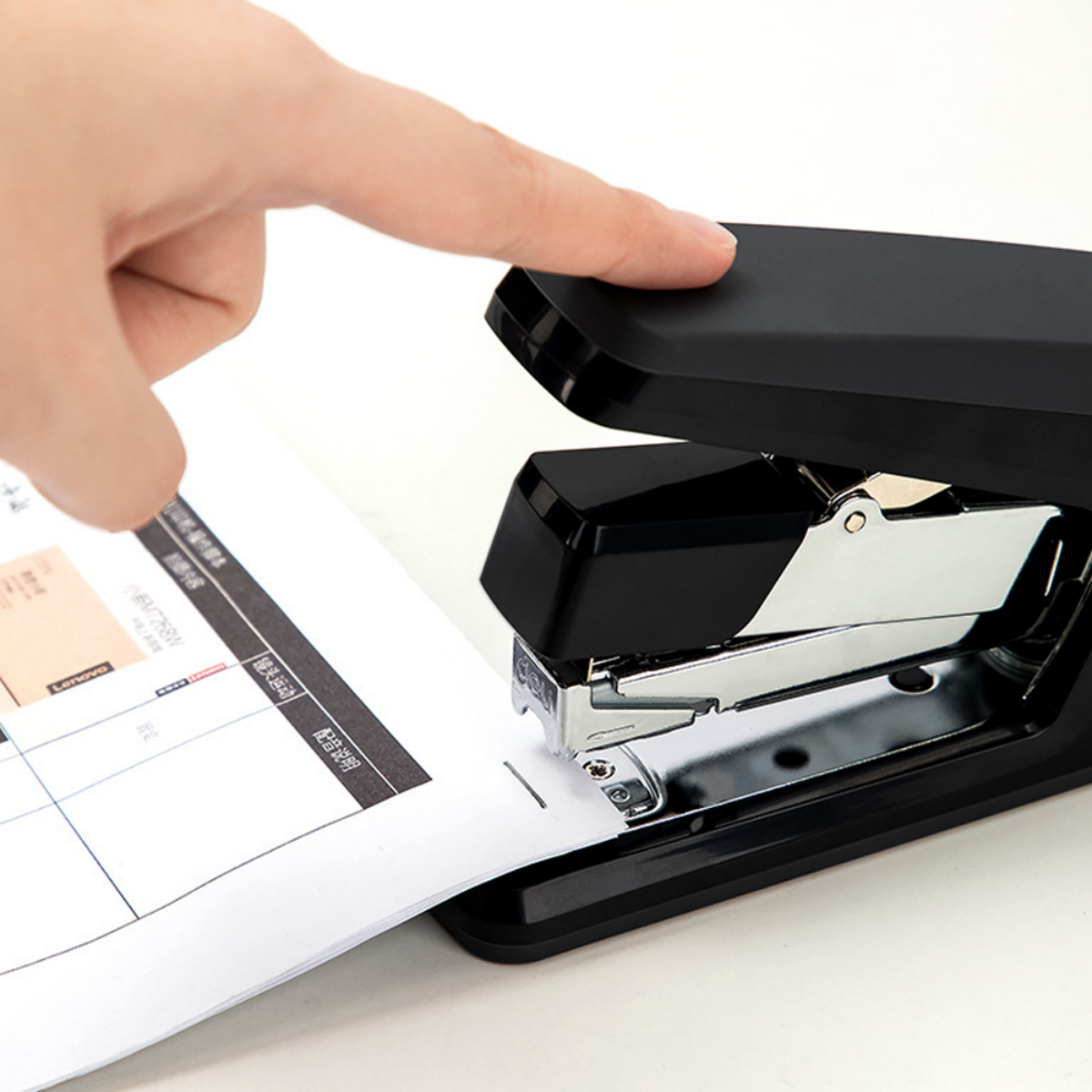 Eine Hand drückt auf einen schwarzen Tacker und heftet weißes Papier zusammen.