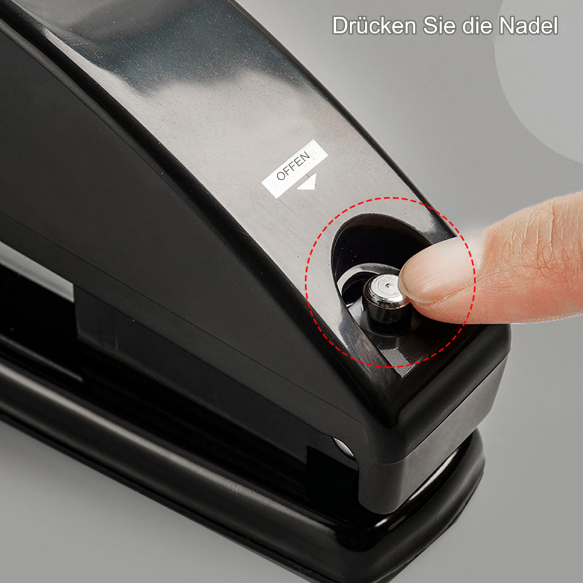 Schwarzer Locher, ein Finger drückt die Nadel. Text: „Drücken Sie die Nadel“.