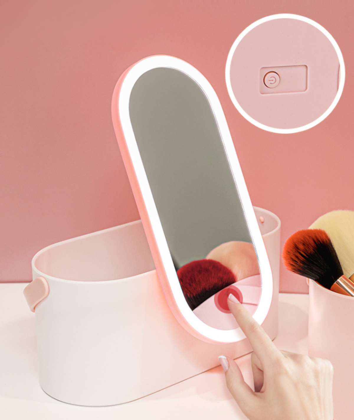 Rosa Schminkspiegel mit LED-Lichtern. Ein Finger berührt einen Power-Button. Make-up-Pinsel stehen daneben.