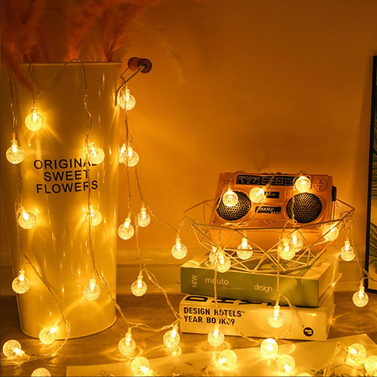 Lichterkette mit durchsichtigen Glühbirnen in einer weißen Vase. Bücher und ein Radio sind sichtbar.