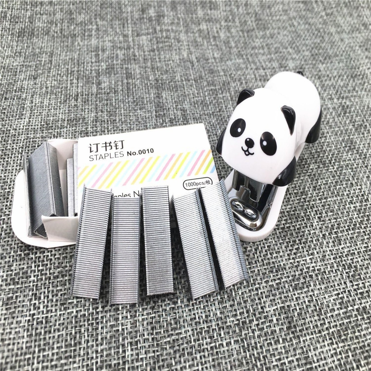 Panda-Tacker neben Heftklammern. Der Tacker und die Heftklammern befinden sich auf einer strukturierten grauen Oberfläche.