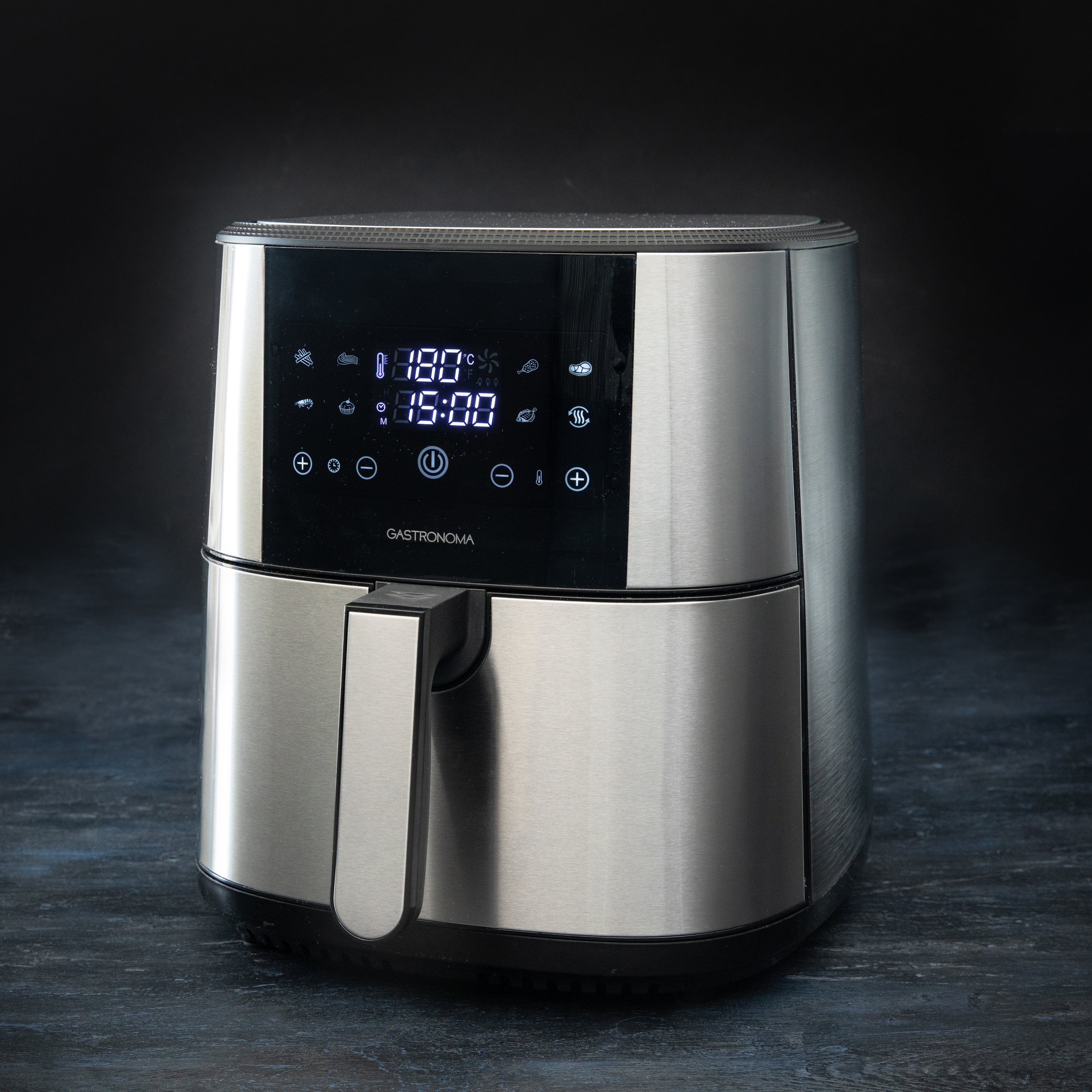 A silver air fryer with a digital display, on a dark surface. The display shows temperature and time settings.