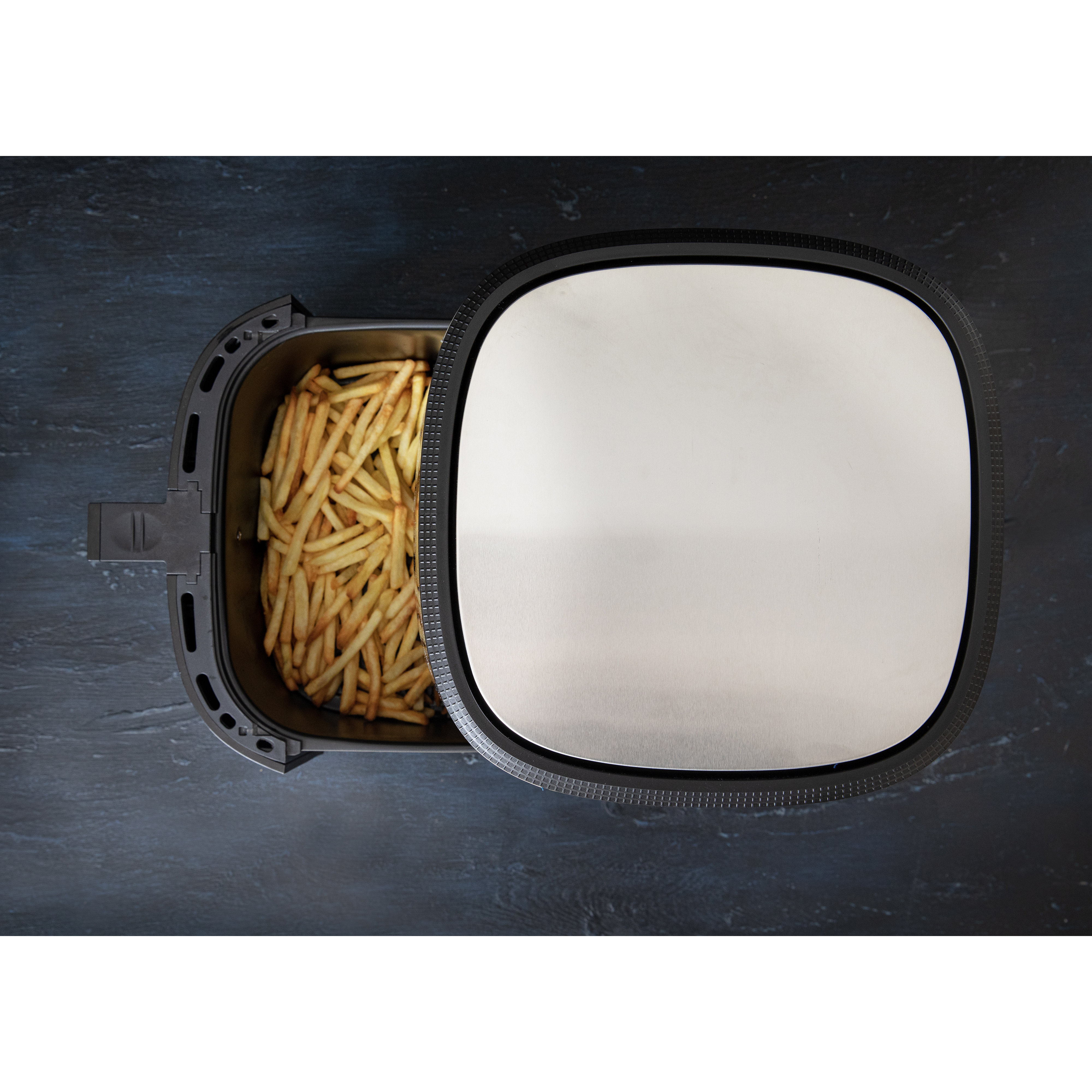 Air fryer with open lid and fries inside. Black appliance. Dark surface. Top view.