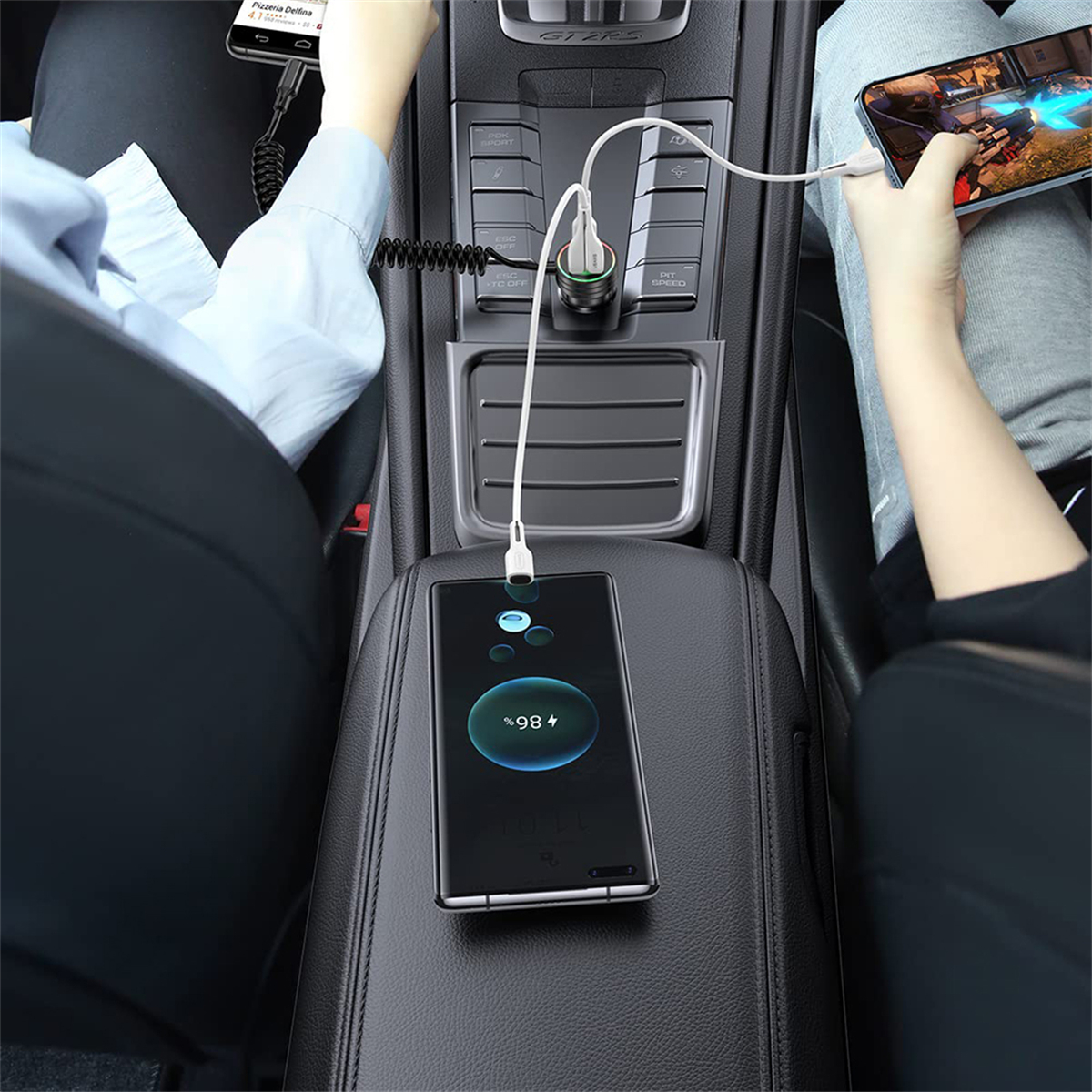 Zwei Personen laden im Auto Handys auf. Einer spielt ein Spiel. Ein Handy zeigt 98 % Ladung.