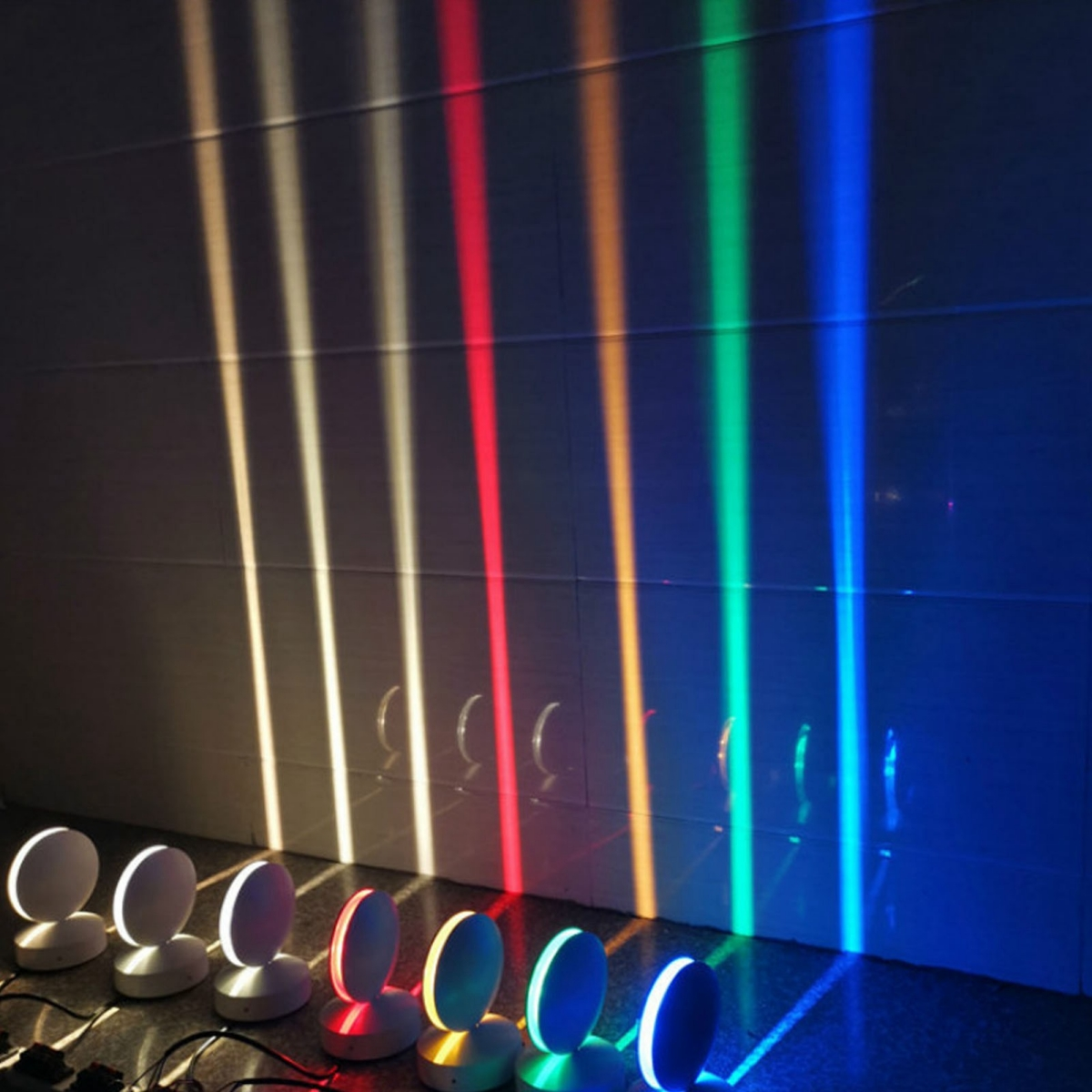Farbige Lichtstrahlen scheinen auf eine Wand. Die Lichter sind rot, orange, gelb, grün und blau.