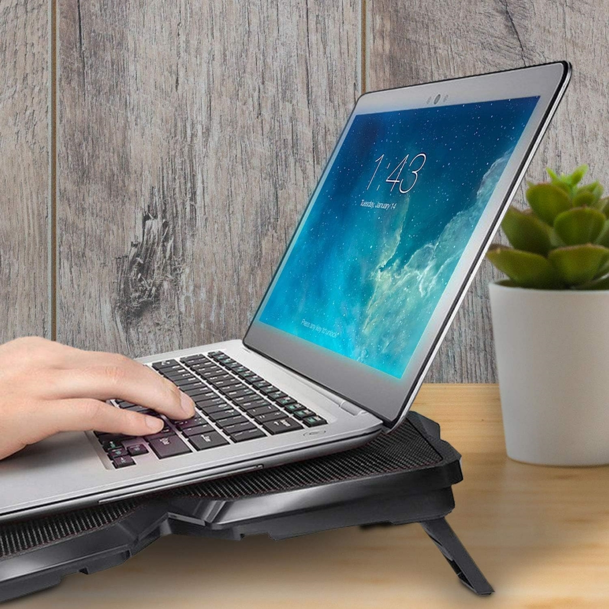 Laptop auf einem schwarzen Ständer, mit einer Person, die ihn benutzt. Hintergrund: Holztisch.