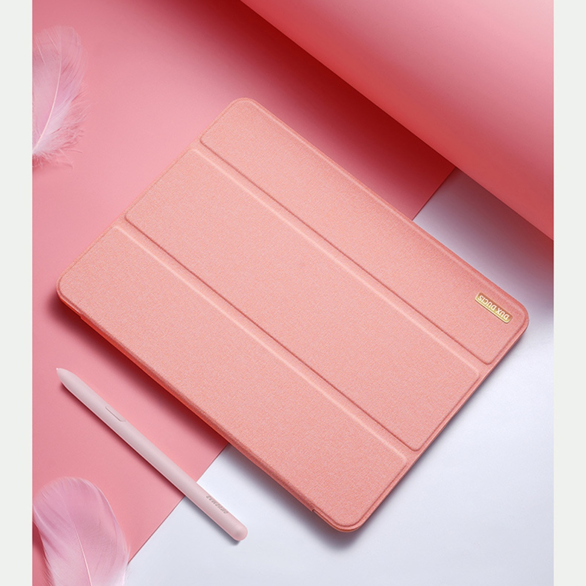 Eine offene rosa Tablethülle mit einem Eingabestift daneben. Weißer Hintergrund. Die Hülle liegt auf einer rosa Oberfläche.