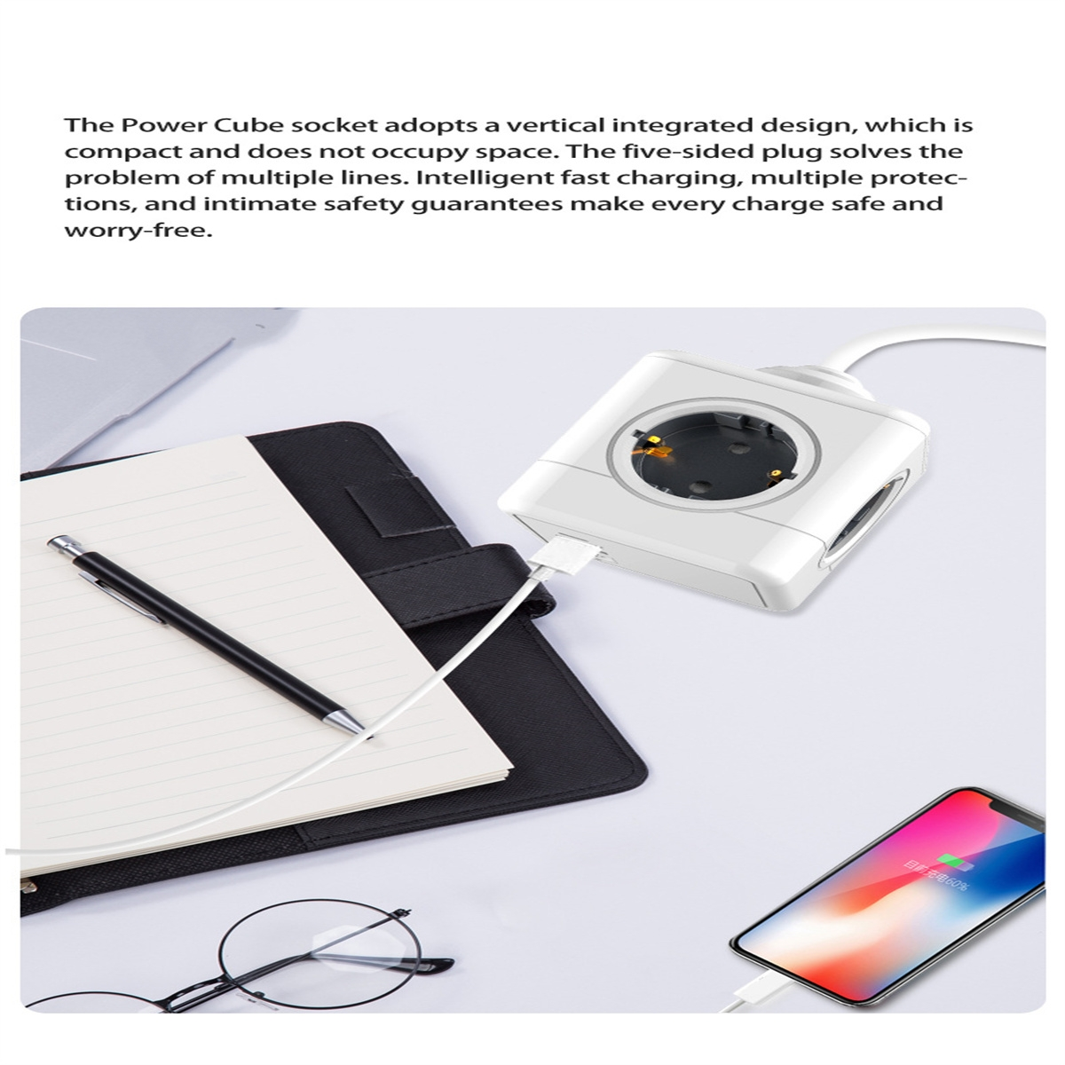 Weißer Power-Cube mit drei Steckdosen, Notizblock, Stift, Telefon, das geladen wird, und Brille auf dem Tisch.