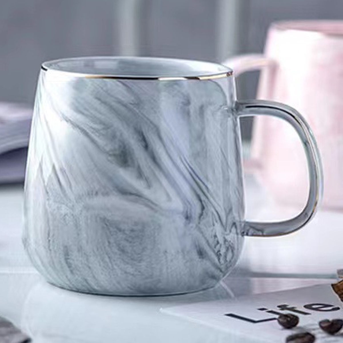 Eine weiß-grau marmorierte Tasse mit Goldrand. Kaffeebohnen und eine Notiz daneben.