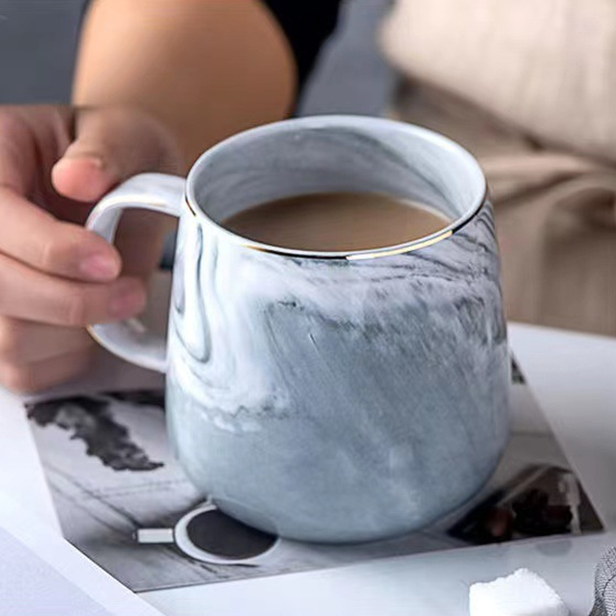 Eine marmorierte Tasse mit Goldrand und eine Hand, die sie hält.