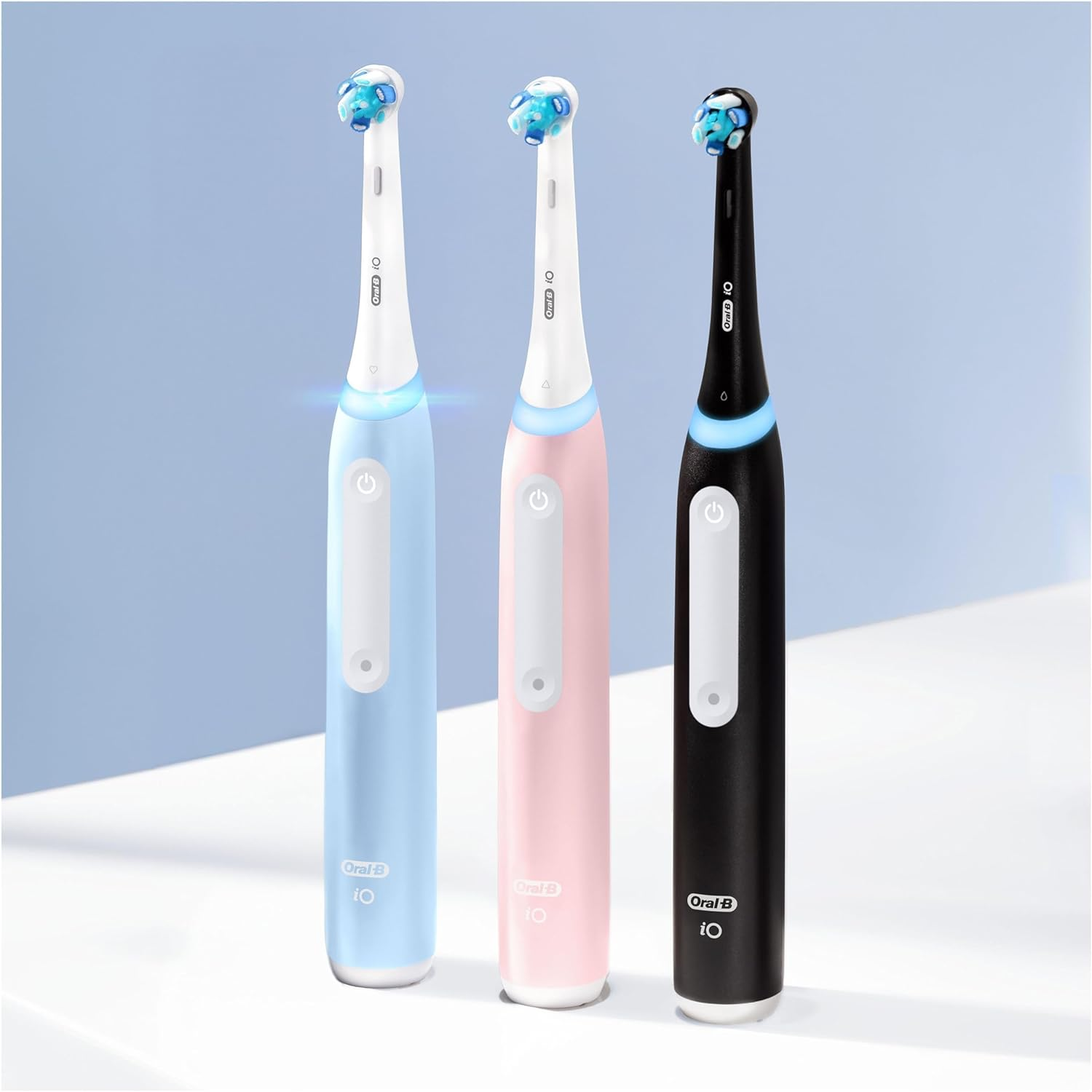 Drei elektrische Zahnbürsten in Blau, Rosa und Schwarz, mit Ladestationen. Oral-B Logo sichtbar.