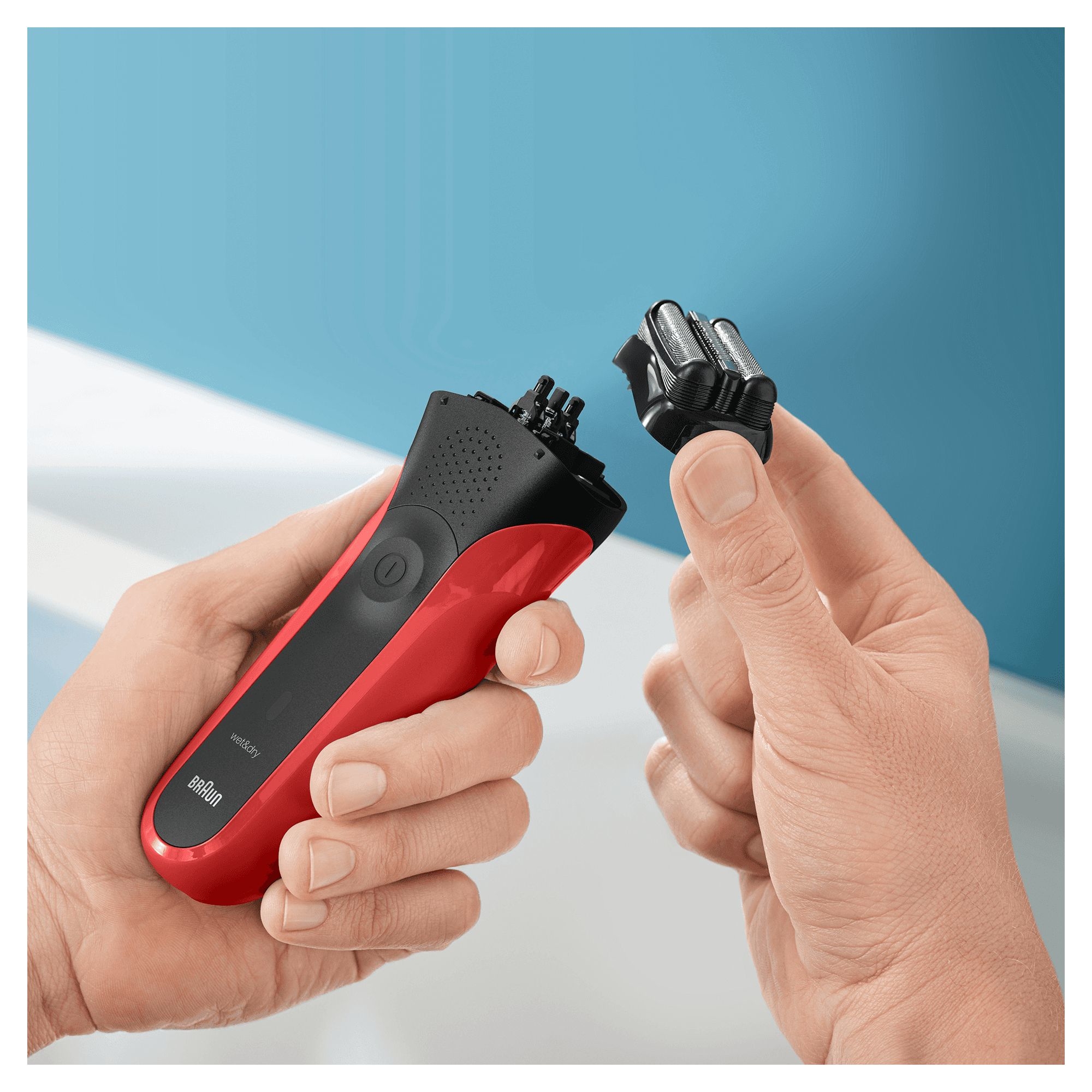 Manos sosteniendo una afeitadora eléctrica roja y negra, con cabezal desmontado.