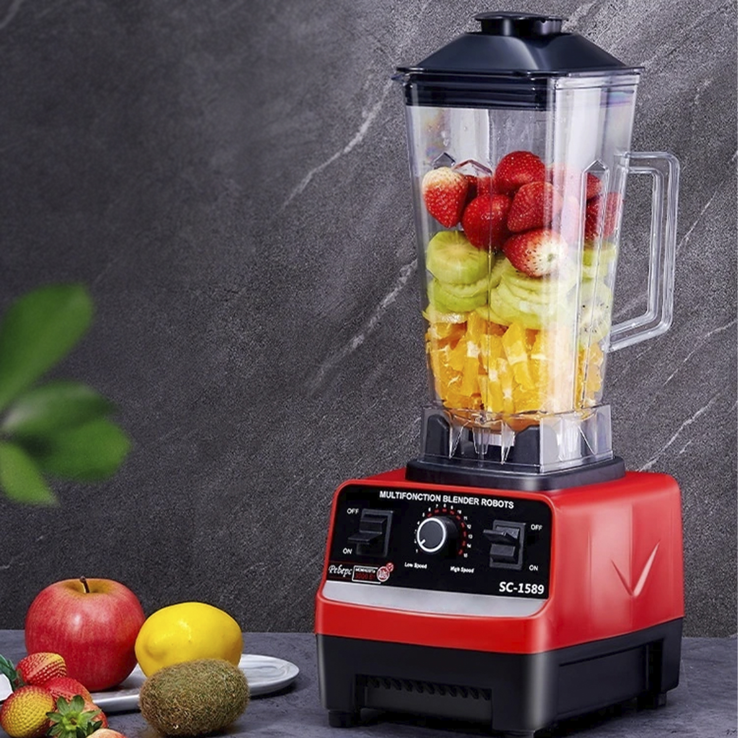 Roter und schwarzer Mixer mit Früchten gefüllt, auf grauem Hintergrund.