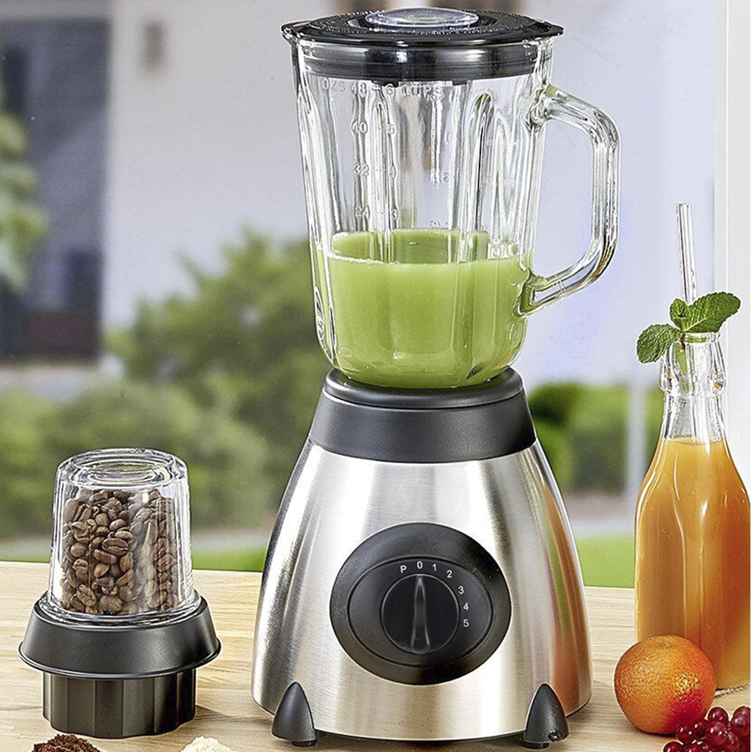 Un frullatore con un barattolo di vetro contenente liquido verde, un barattolo più piccolo di chicchi di caffè e succo d'arancia.