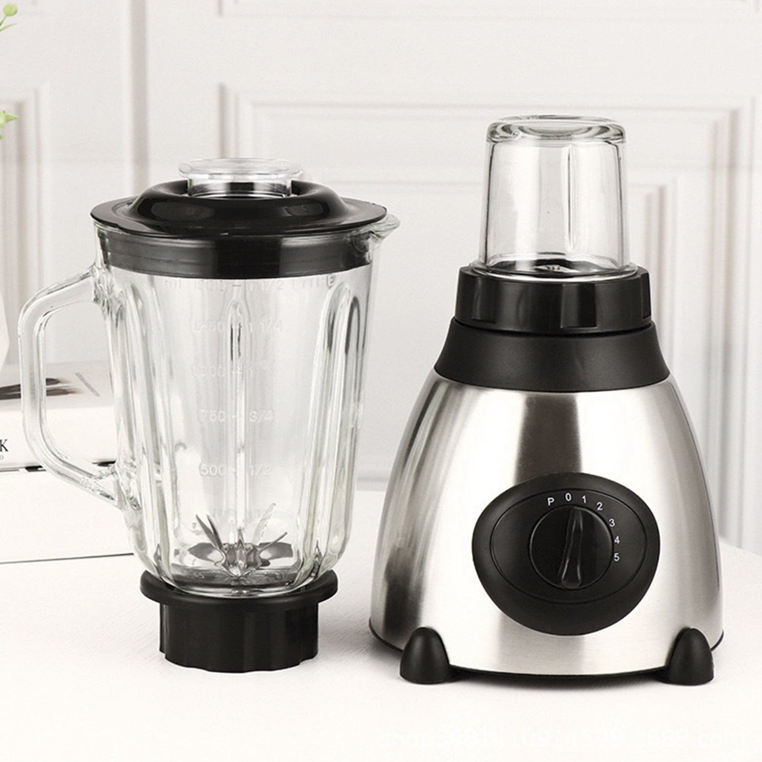 Frullatore con caraffa in vetro e base in acciaio inox. Coperchio nero e manopola di controllo. Sfondo bianco.