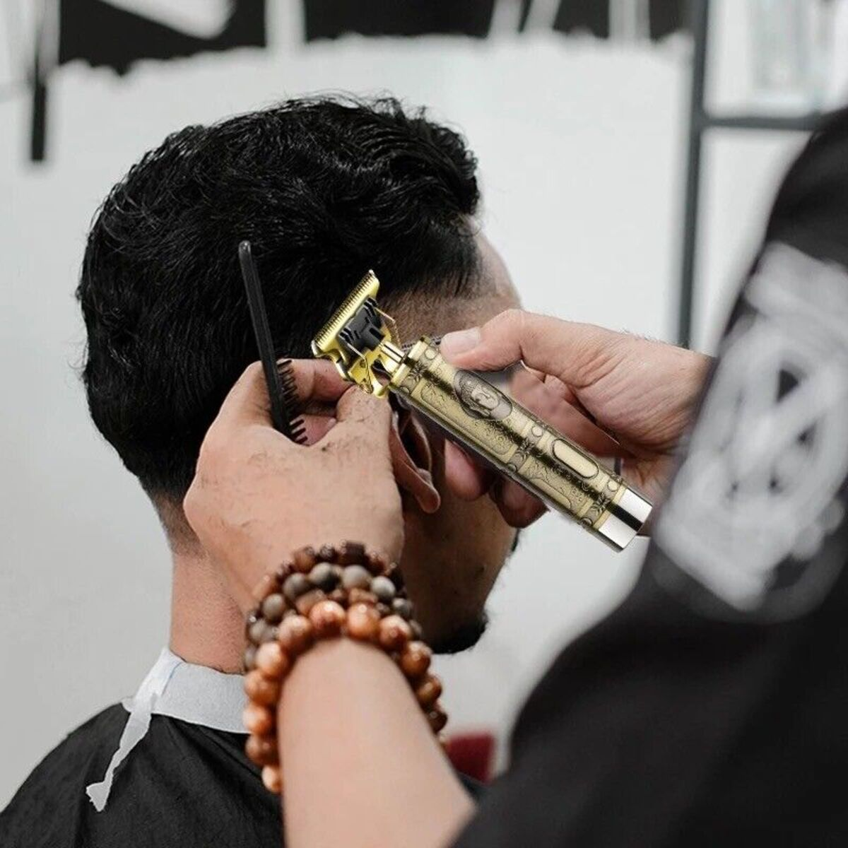 Ein Friseur benutzt einen goldfarbenen Haarschneider, um das Haar eines Mannes zu schneiden. Ein Kamm wird benutzt.