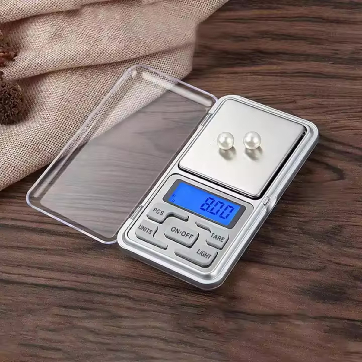 Digitale Taschenwaage mit zwei Perlen auf der Wiegefläche, einem durchsichtigen Deckel, auf Holz.