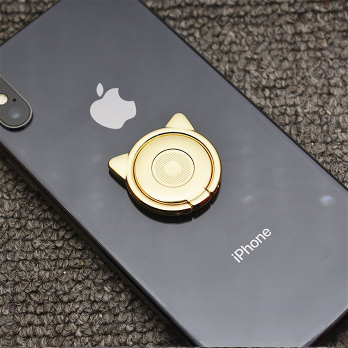 Goldener katzenförmiger Telefonhalter auf einem schwarzen iPhone. Der Hintergrund ist eine strukturierte graue Oberfläche.