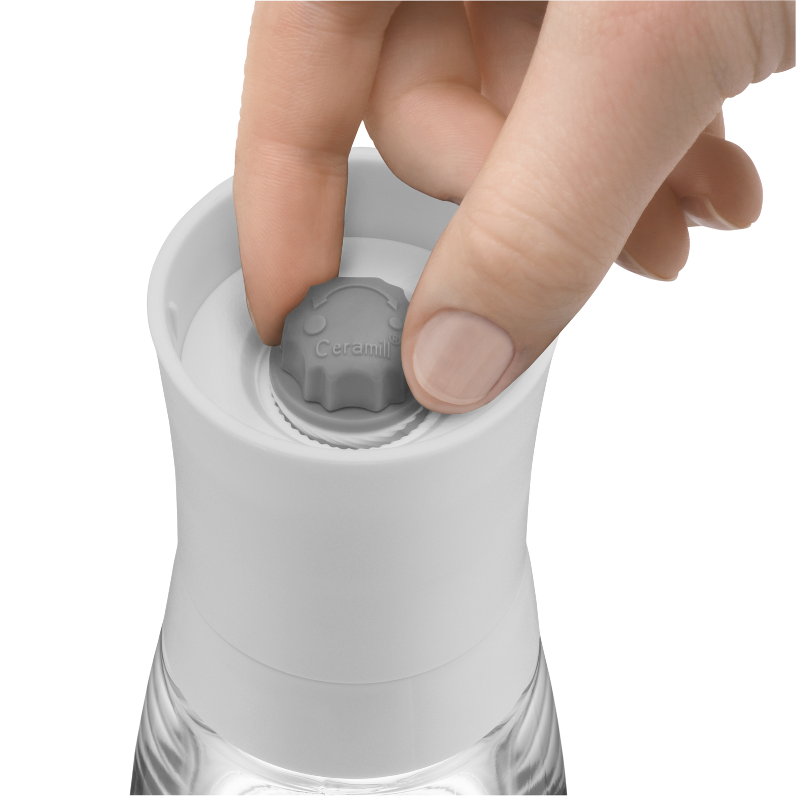 Die Hand einer Person dreht einen grauen Drehknopf an einer weißen und gläsernen Pfeffermühle. Die Mühle steht vor weißem Hintergrund.