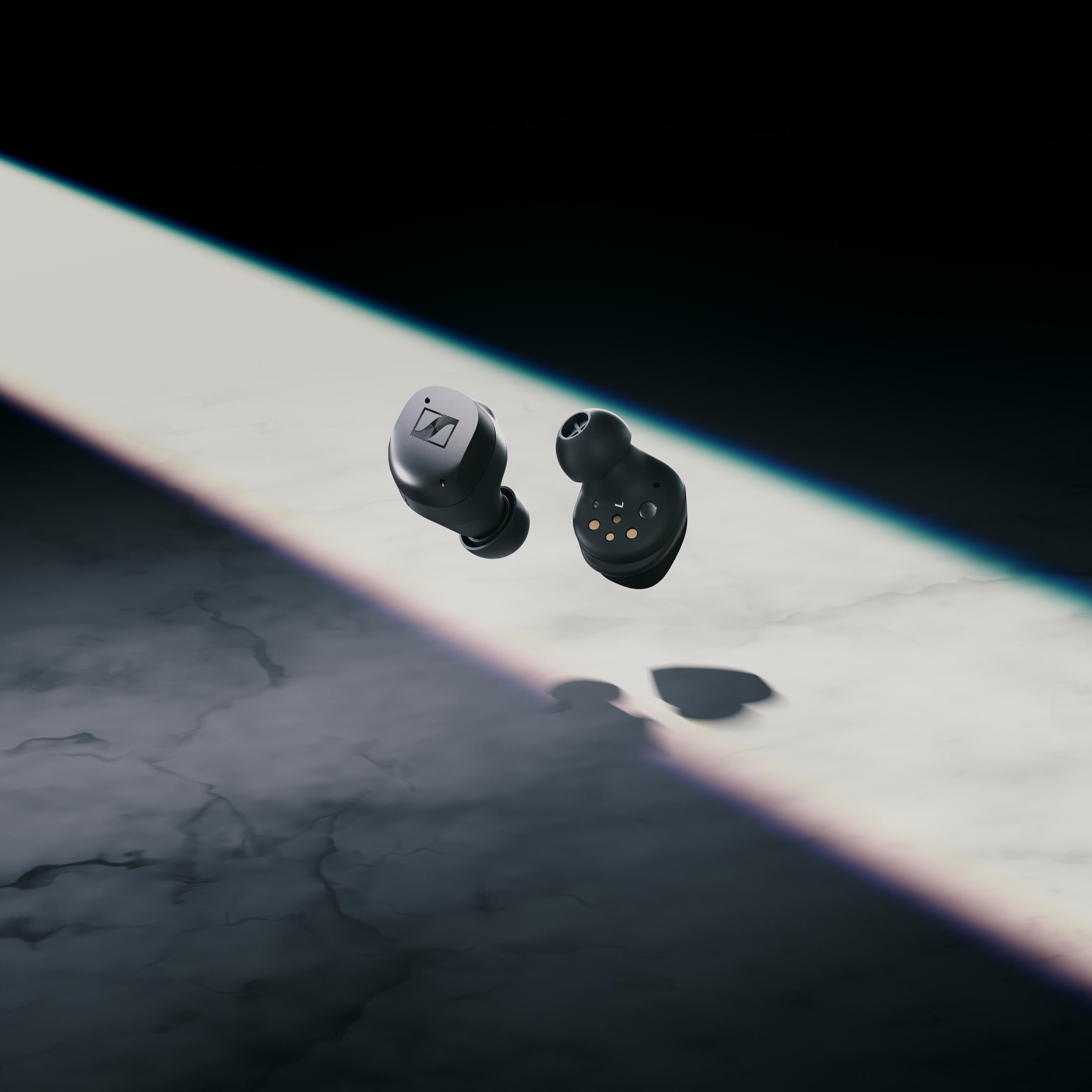 Czarne słuchawki douszne. Dwie słuchawki unoszące się w ciemnym, zacienionym otoczeniu.