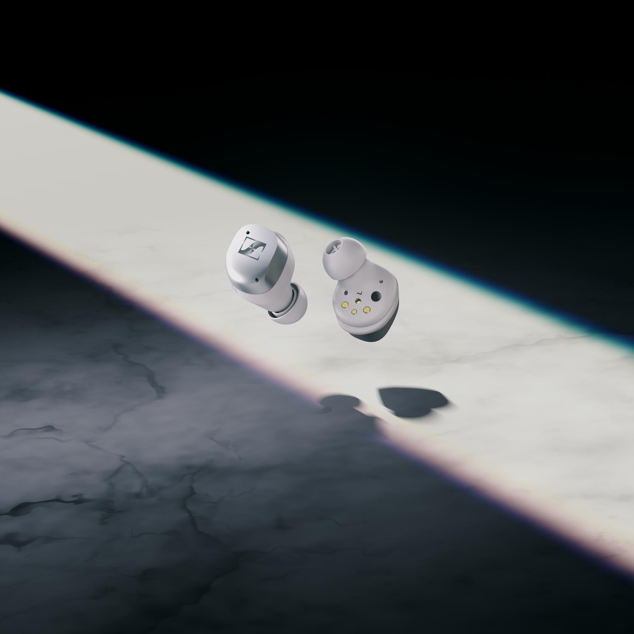Dos auriculares inalámbricos blancos flotando en un rayo de luz. Fondo oscuro.