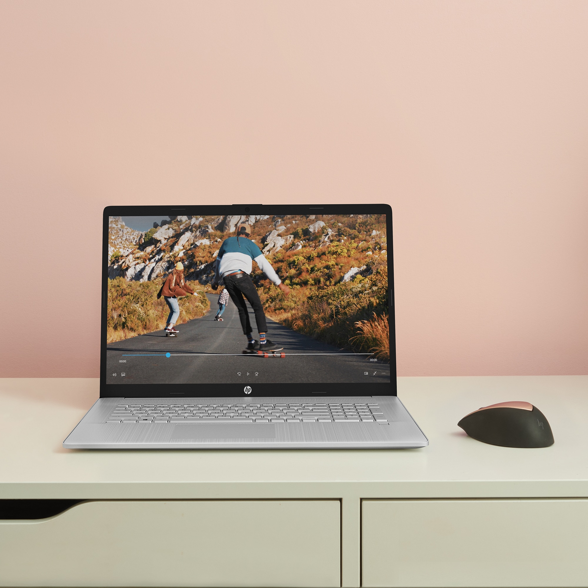 Ein Laptop zeigt ein Video von Skateboardern. Eine Maus liegt auf einem weißen Schreibtisch.