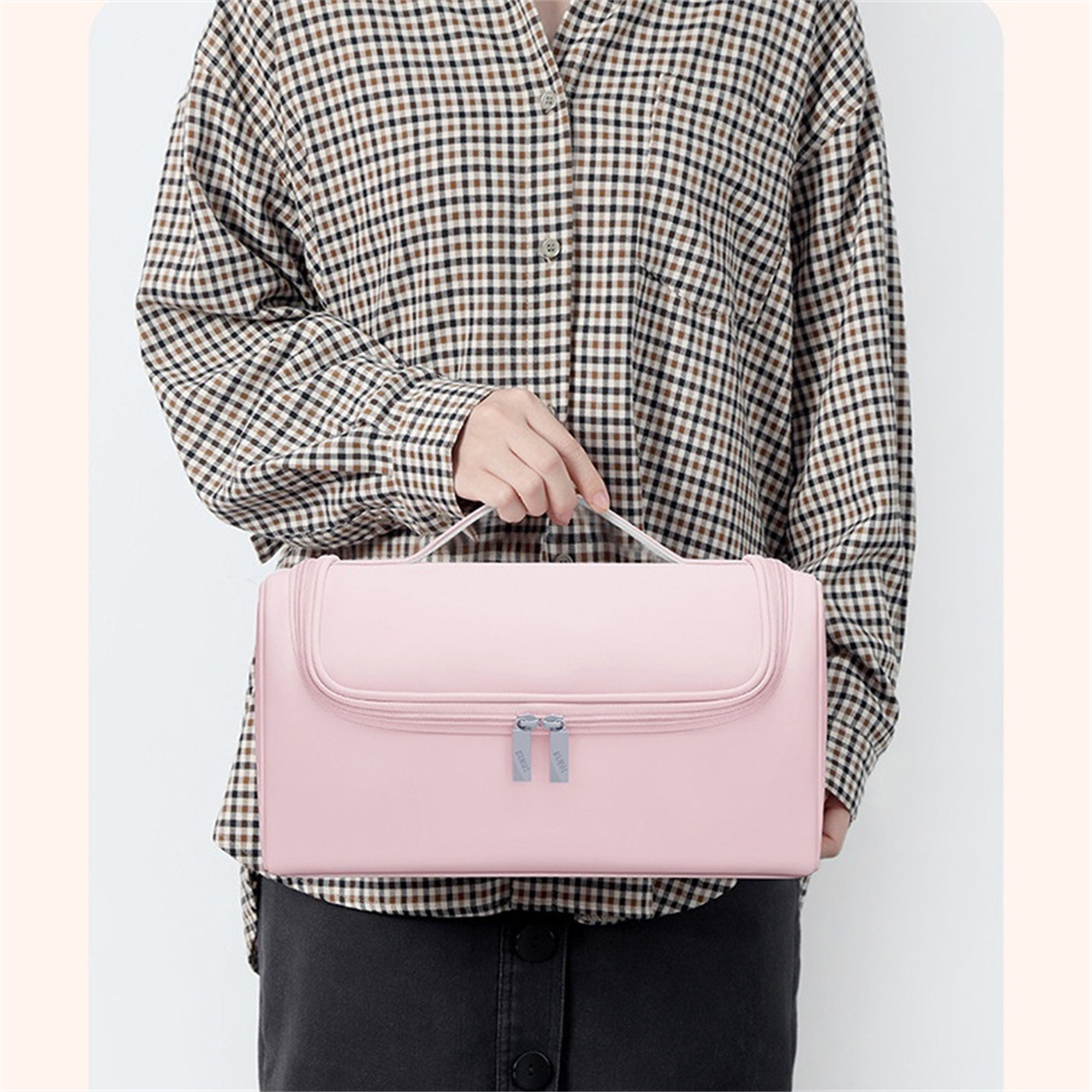 Person hält eine pinkfarbene Hänge-Reisetasche, die Griffe und den Reißverschluss zeigend.