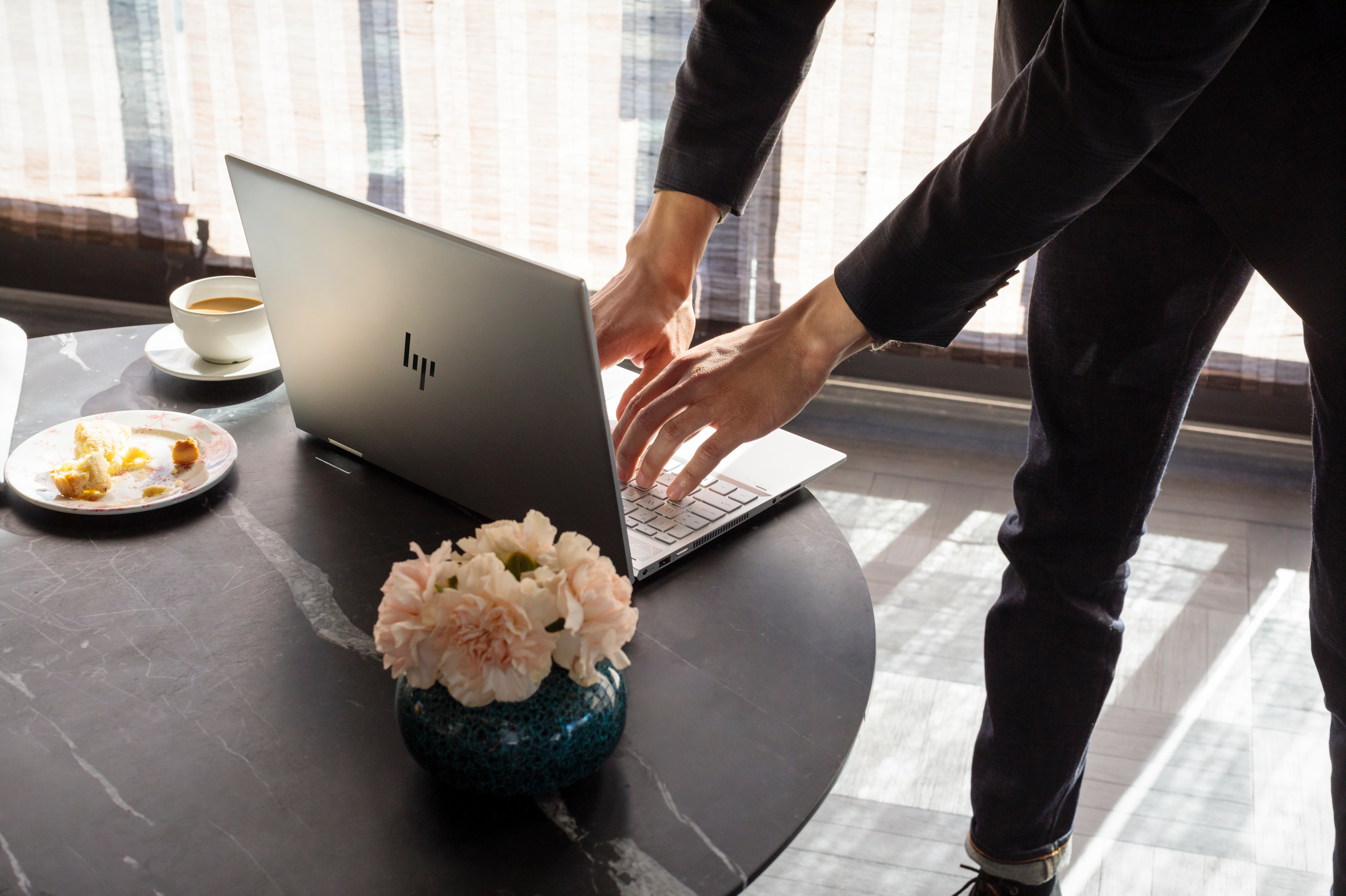 Una persona lavora su un laptop. Fiori e una tazza di caffè su un tavolo.