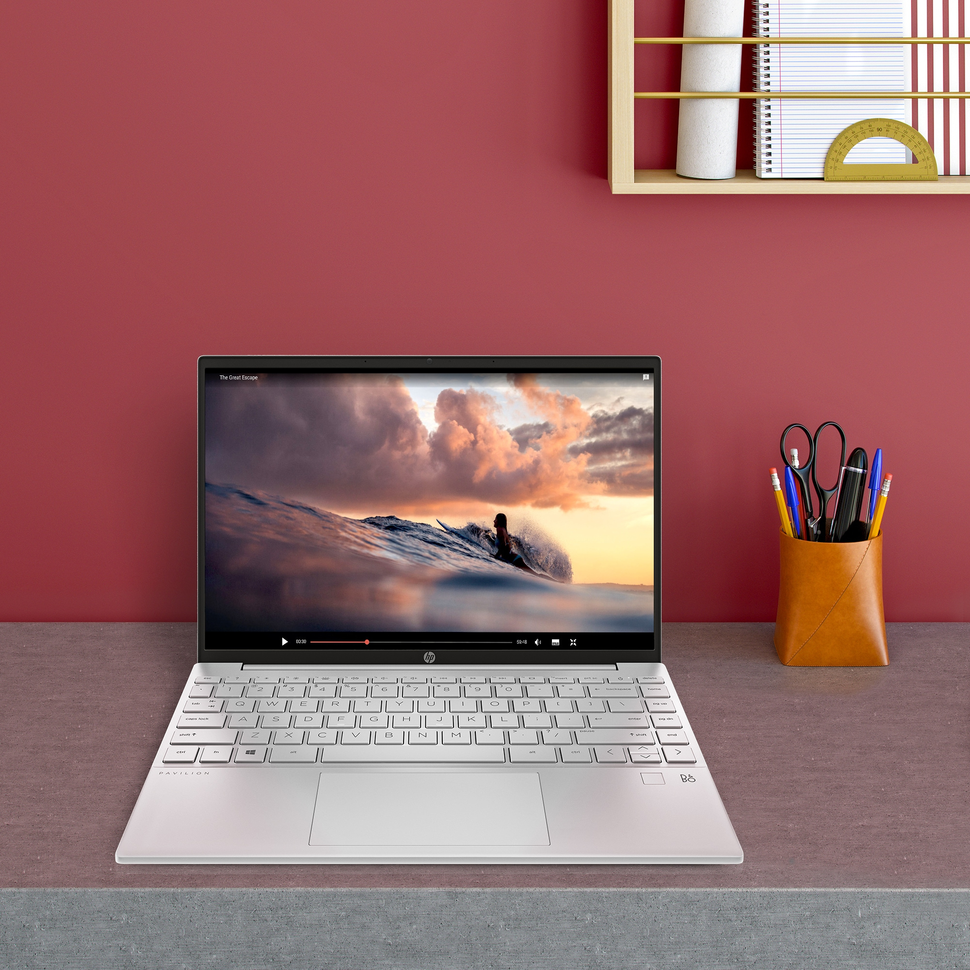 Laptop HP bianco aperto su scrivania, video in riproduzione. Parete rossa, matite.