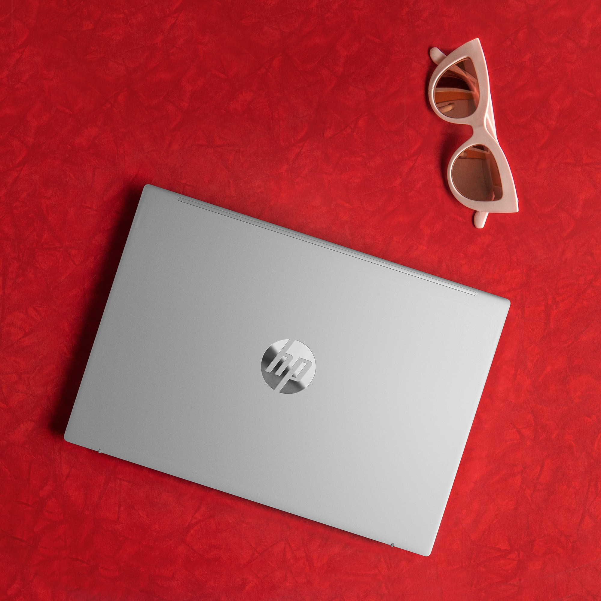Laptop argentato chiuso su superficie rossa. Occhiali da sole sulla superficie.