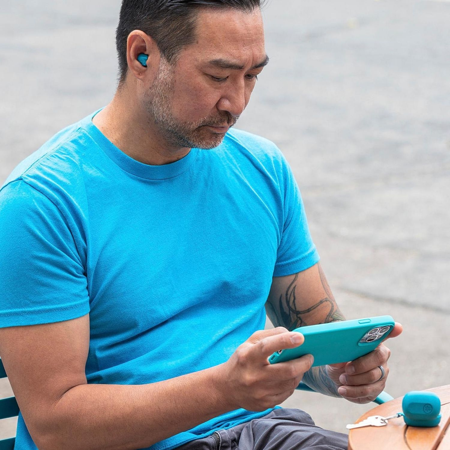 Hombre con auriculares mira un teléfono. Se ven una funda de teléfono turquesa, una mesa y auriculares.