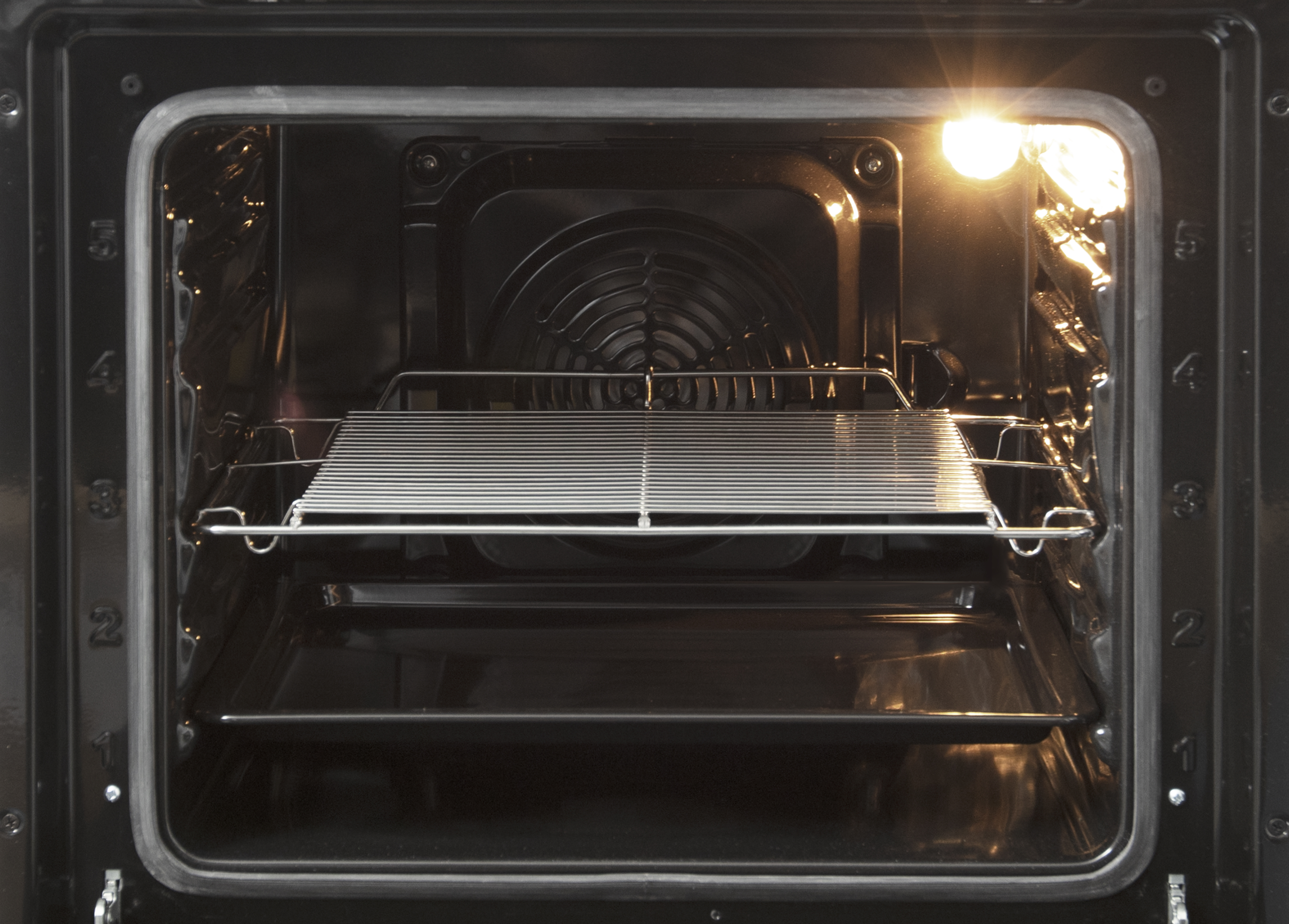 Binnenkant van een oven met een rek en een bakplaat. De oven is verlicht.