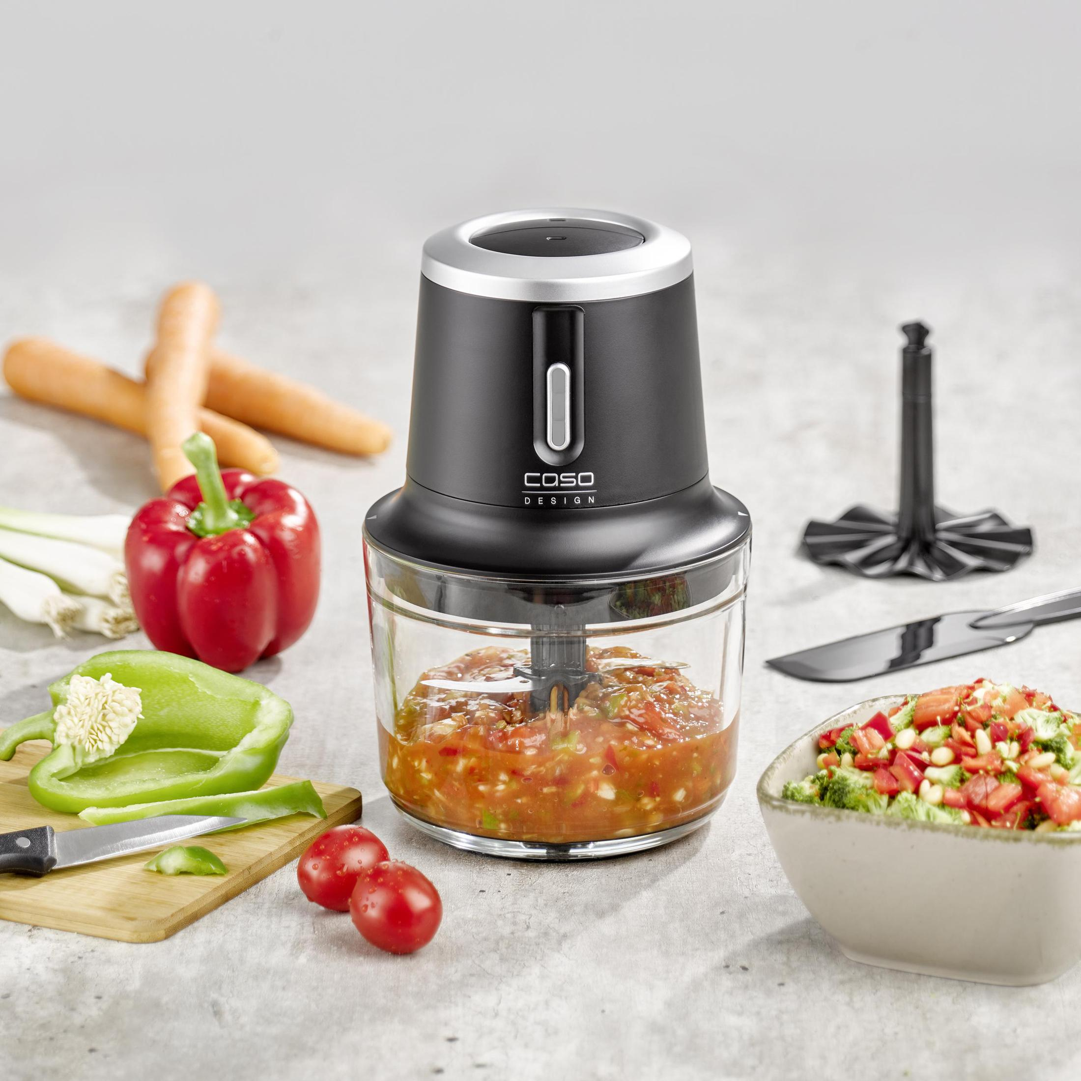 Tritatutto nero con ingredienti, tra cui verdure, su sfondo grigio.