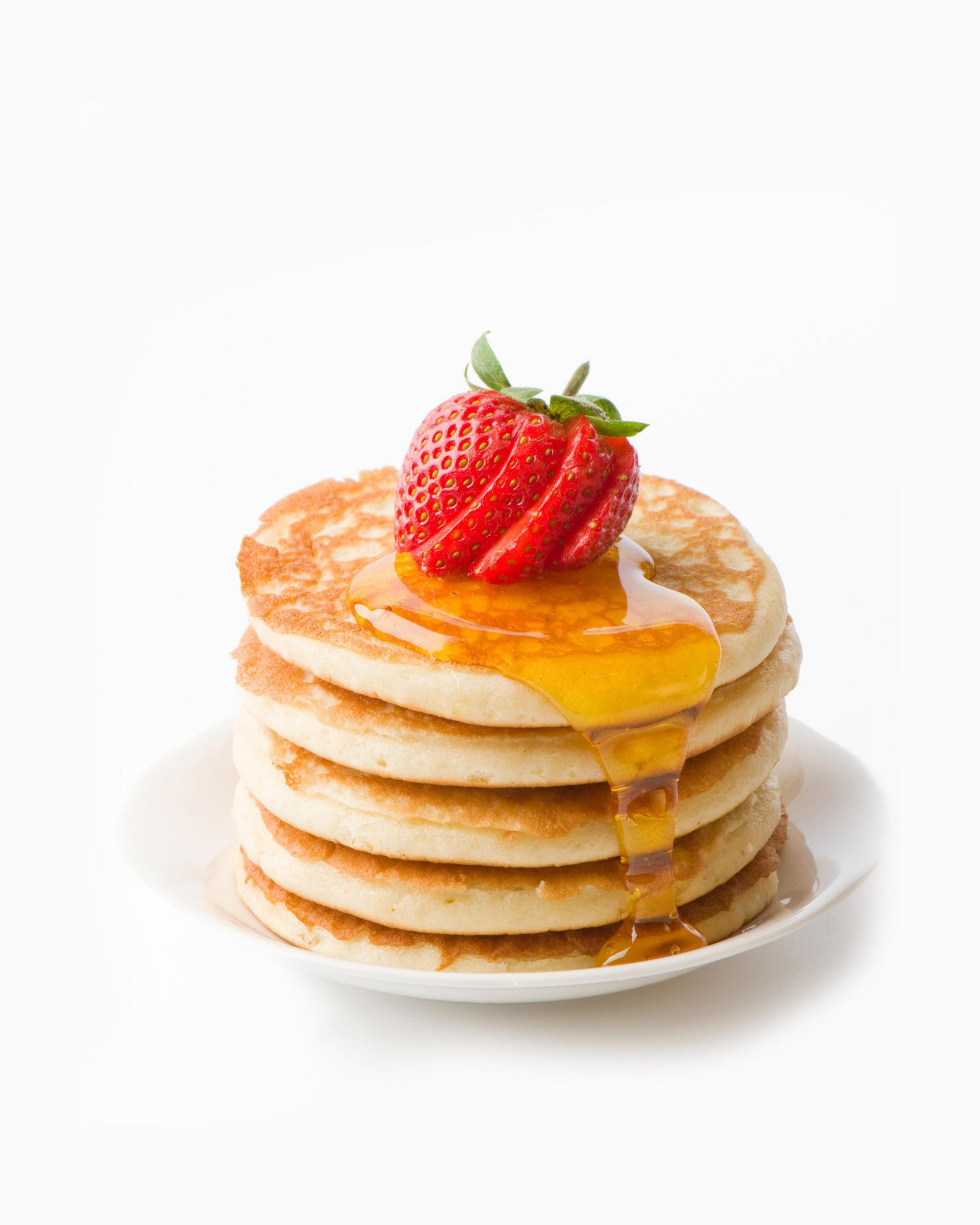 Stos naleśników z syropem i truskawką na wierzchu, na białym talerzu, na białym tle.