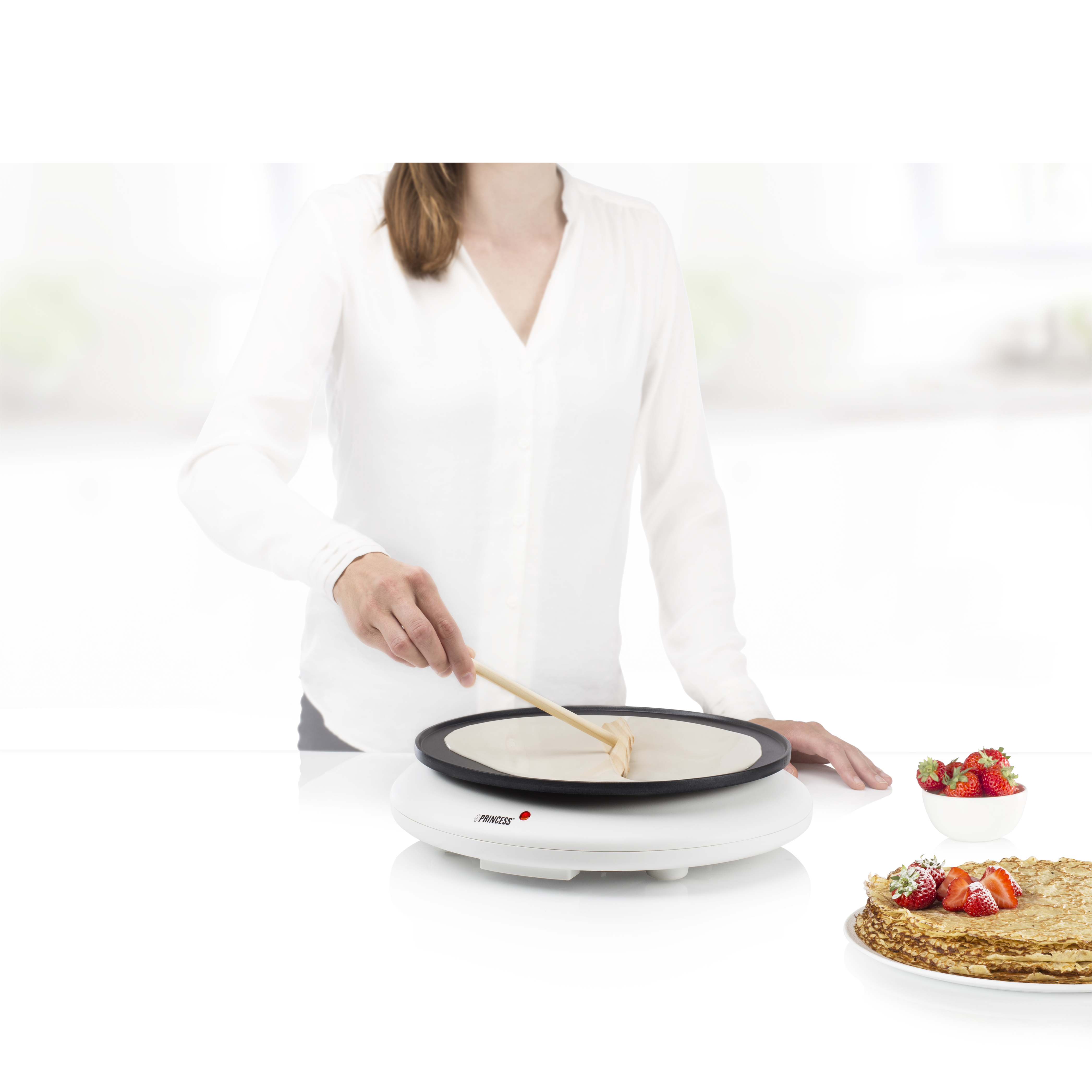 Donna che fa pancake su un elettrodomestico bianco, con fragole.