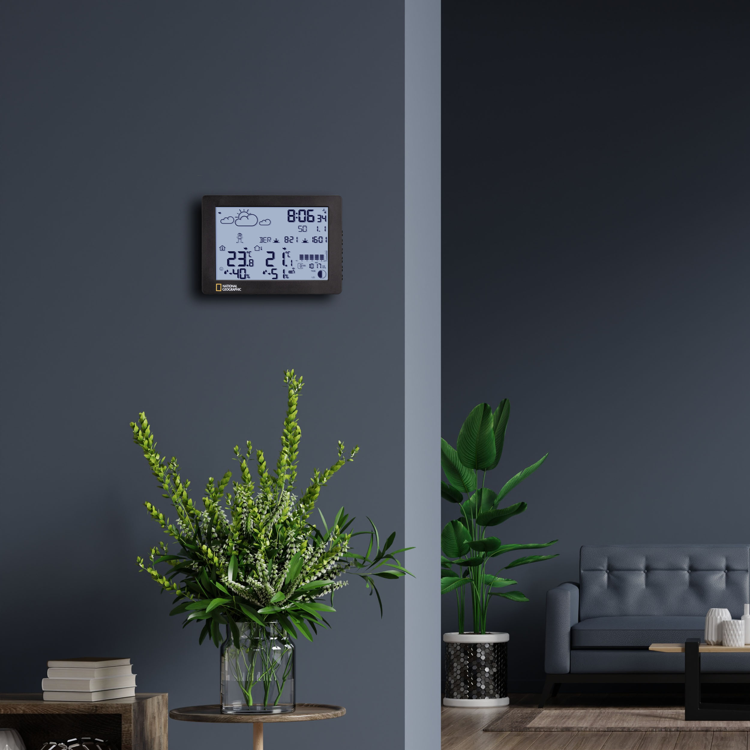 Una habitación con una pared azul oscuro, una estación meteorológica, una planta y un sofá gris. Una mesa de madera en primer plano.