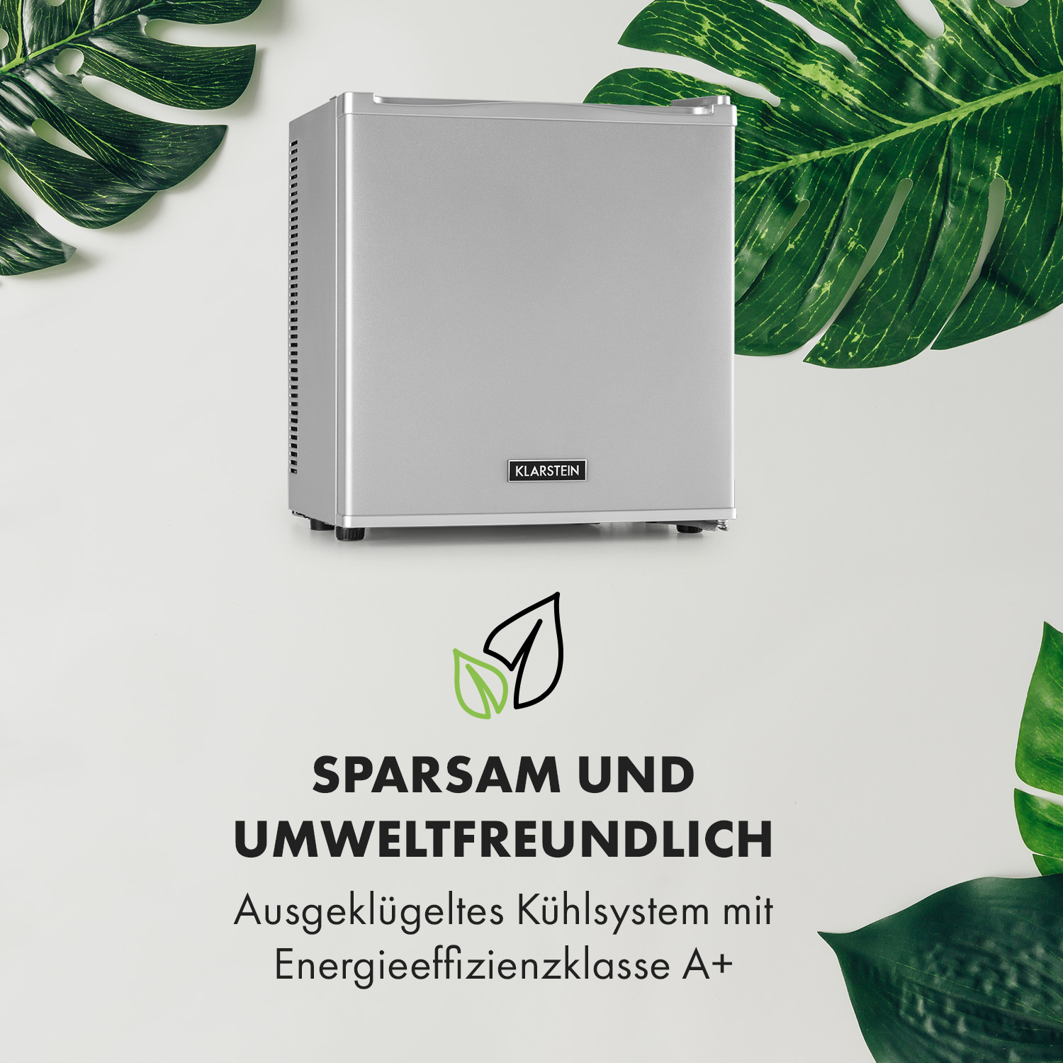 Ein kleiner grauer Kühlschrank mit Text auf der Vorderseite, umgeben von grünen Blättern.