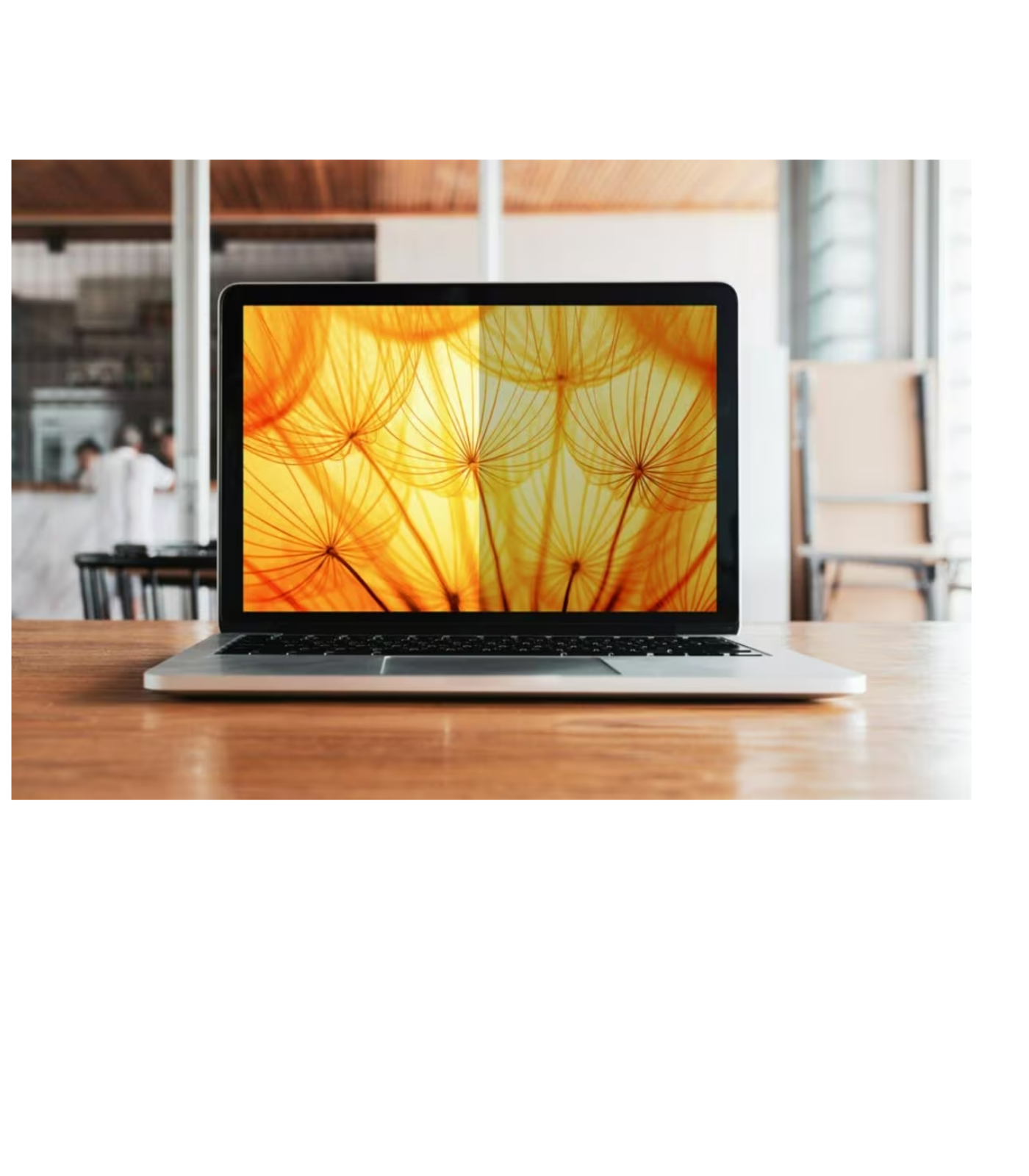 Ein Laptop mit einem gelb-orangen abstrakten Bild auf einem Holztisch, mit verschwommenem Hintergrund.