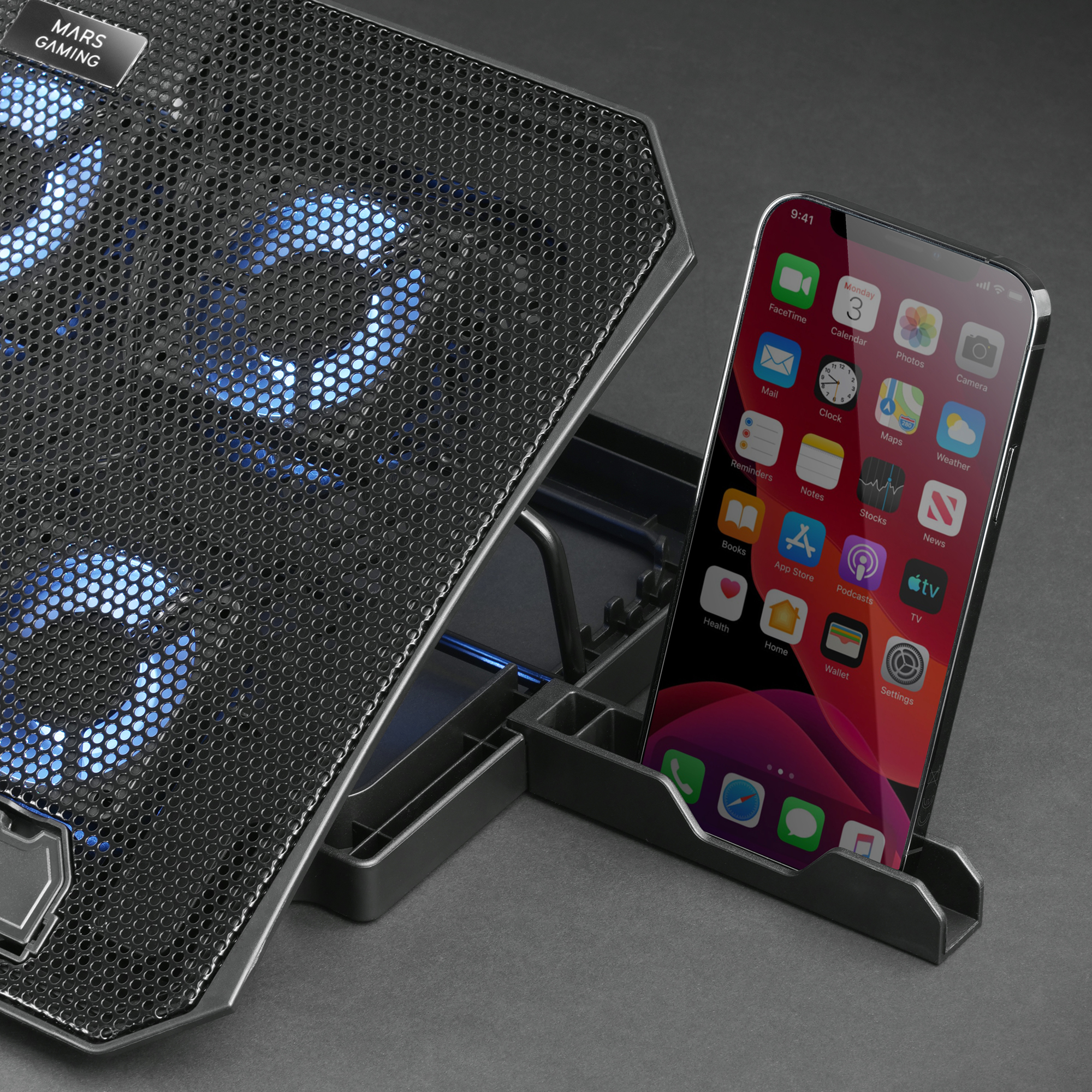 Smartphone en un soporte, junto a una almohadilla de enfriamiento. La almohadilla tiene ventiladores iluminados en azul.