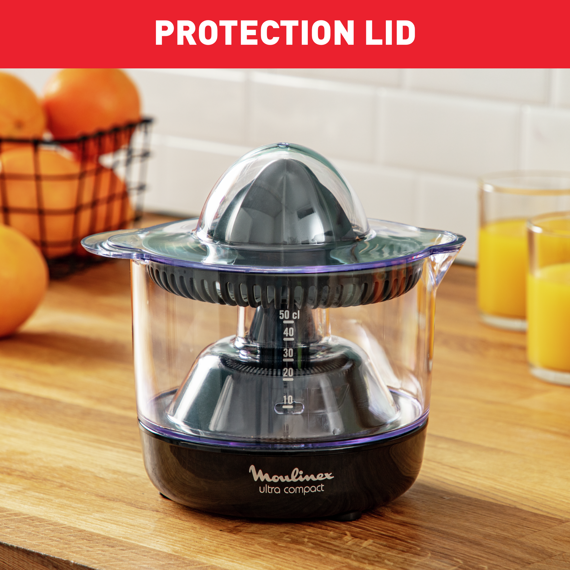 Wyiskark z przezroczystym pojemnikiem, czarną podstawą i ciemną pokrywą, z pomarańczami i szklankami soku.