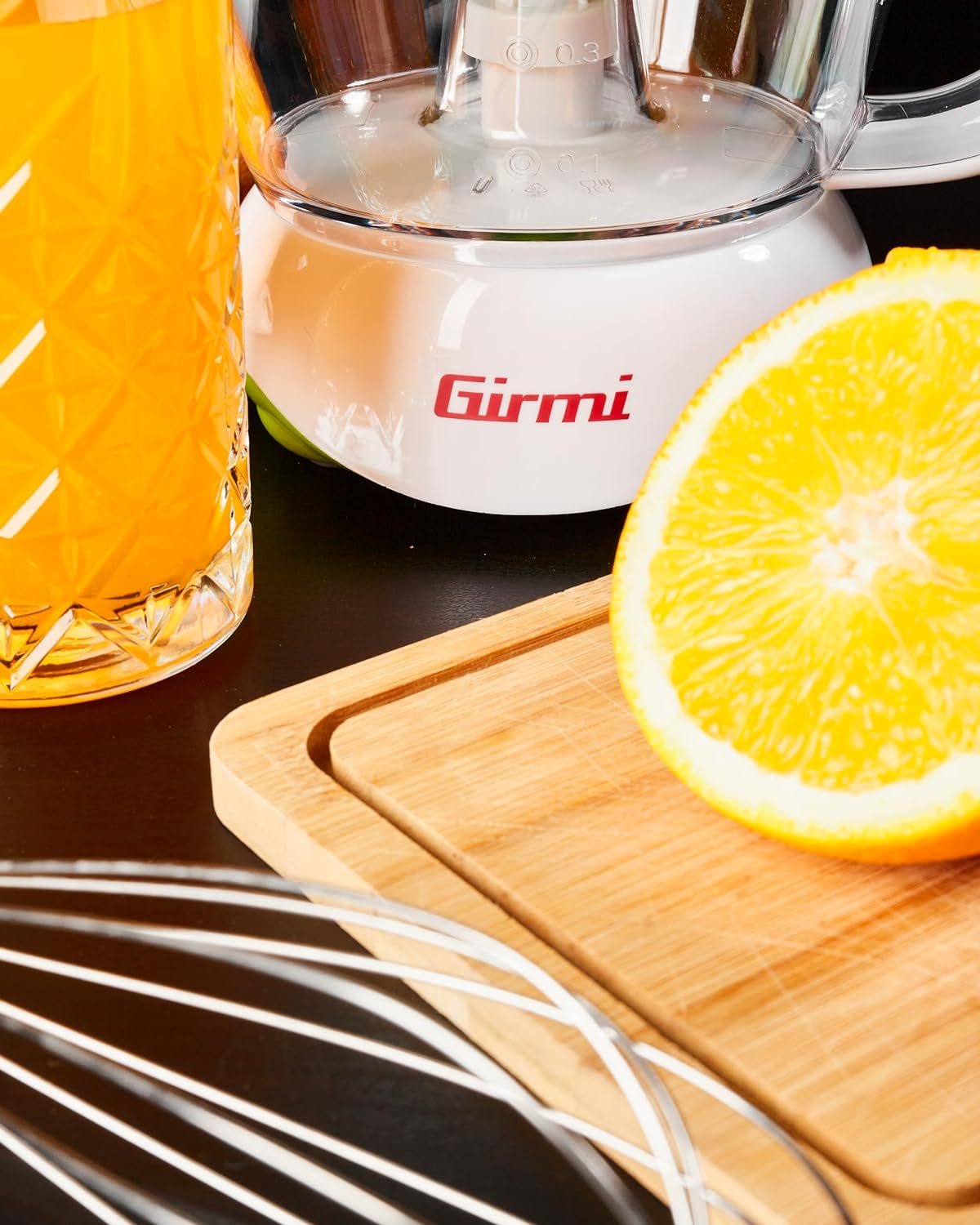 Glas Orangensaft, Entsafter, halbe Orange und Holzbrett auf schwarzer Oberfläche.