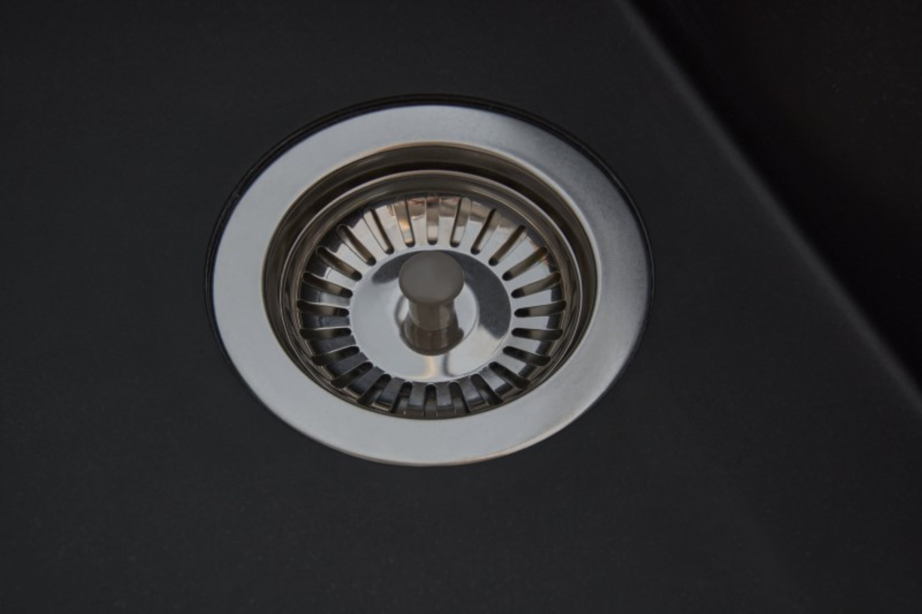 Dettaglio dello scarico del lavandino con filtro metallico lucido in un lavabo scuro.